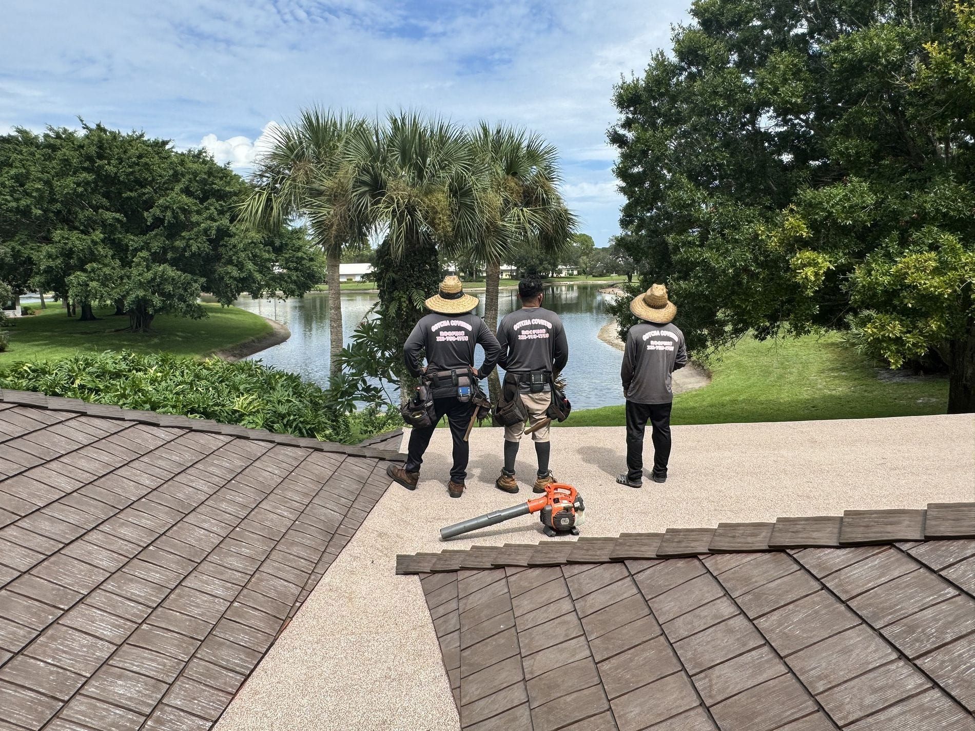 Three men are standing on top of a roof looking at a lake.