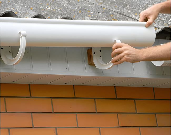 A person is installing a gutter on a brick wall.
