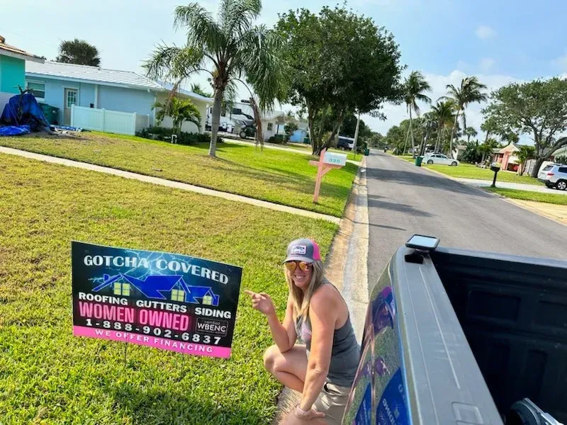 A woman is sitting in the back of a truck holding a sign.