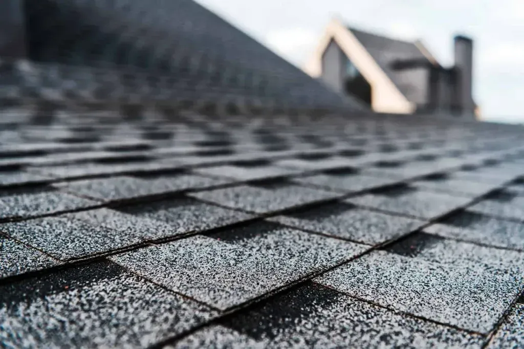 A close up of a roof with shingles and a house in the background.
