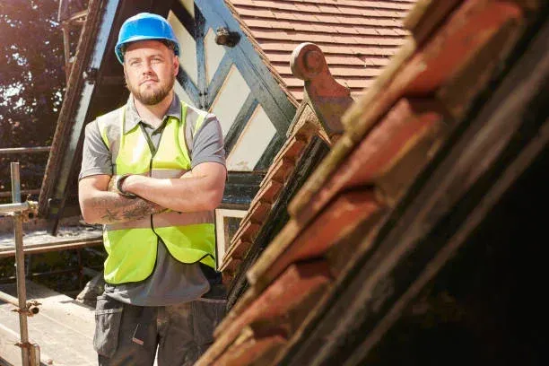 A man wearing a hard hat and safety vest is standing in front of a roof.