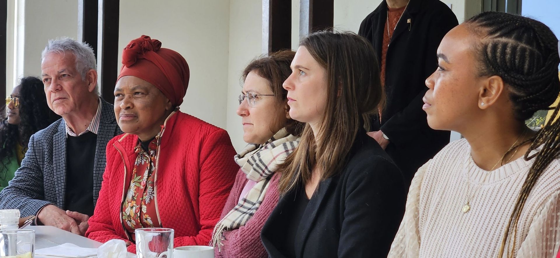 A crowd of people look off to the left, as if listening intently to someone talking.