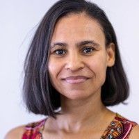 A smiling woman, with short brown hair, wearing a black vest, and a multi-coloured scarf.