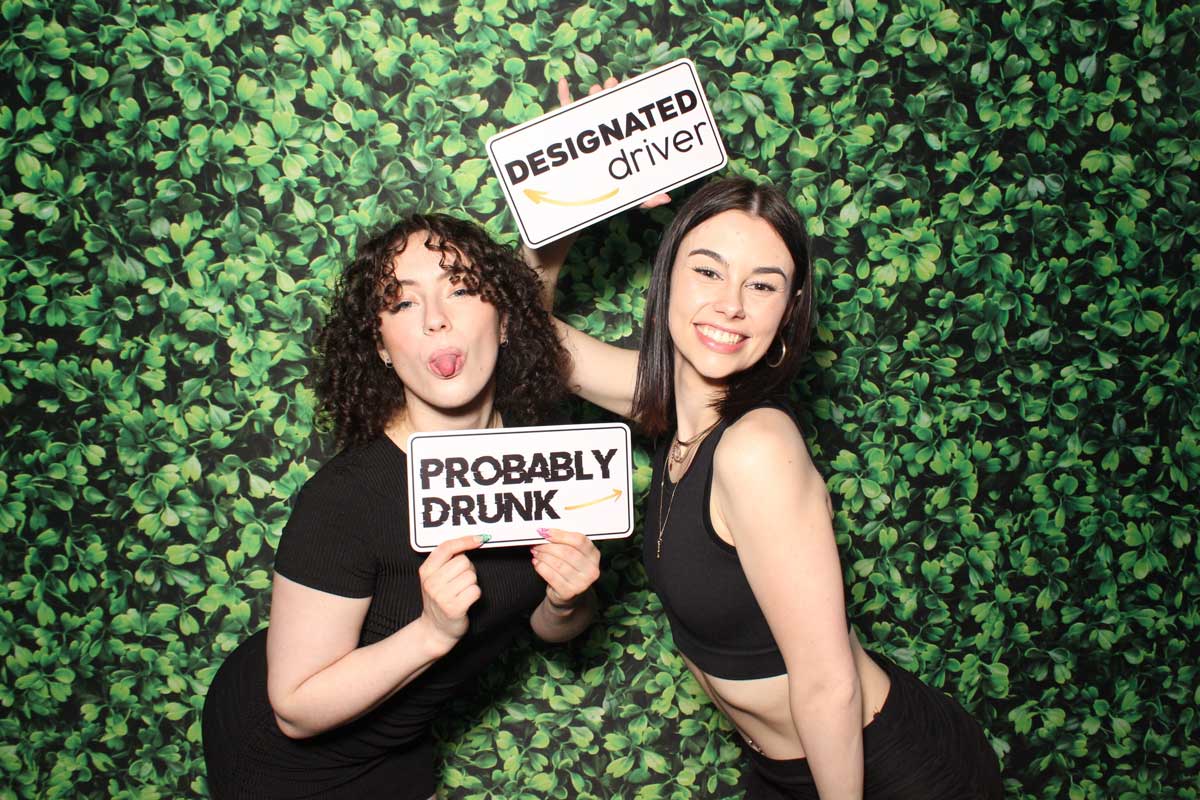 Two women are posing for a picture in a photo booth holding signs.