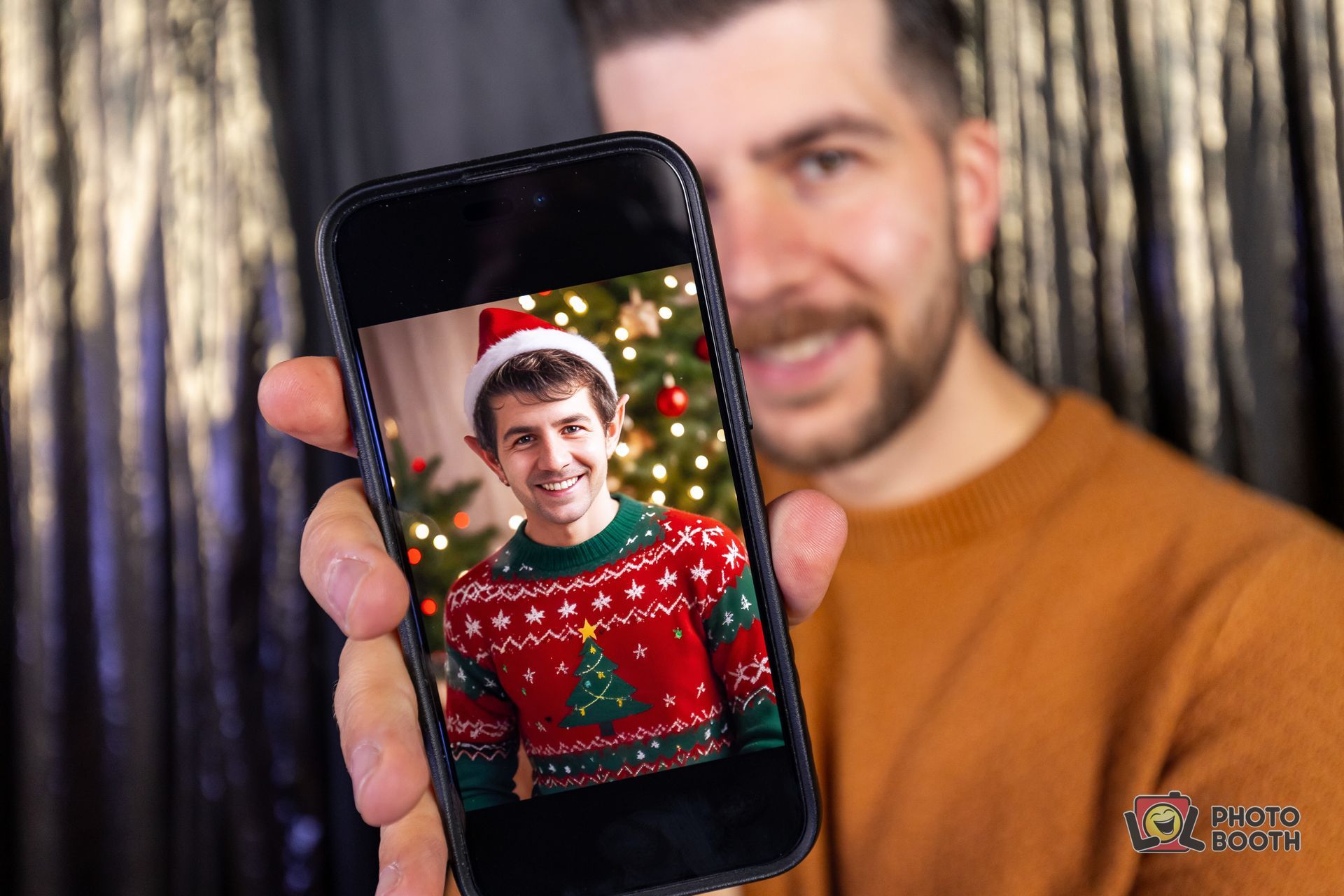 Man holding phone with photo of another man in Christmas sweater, smiling.