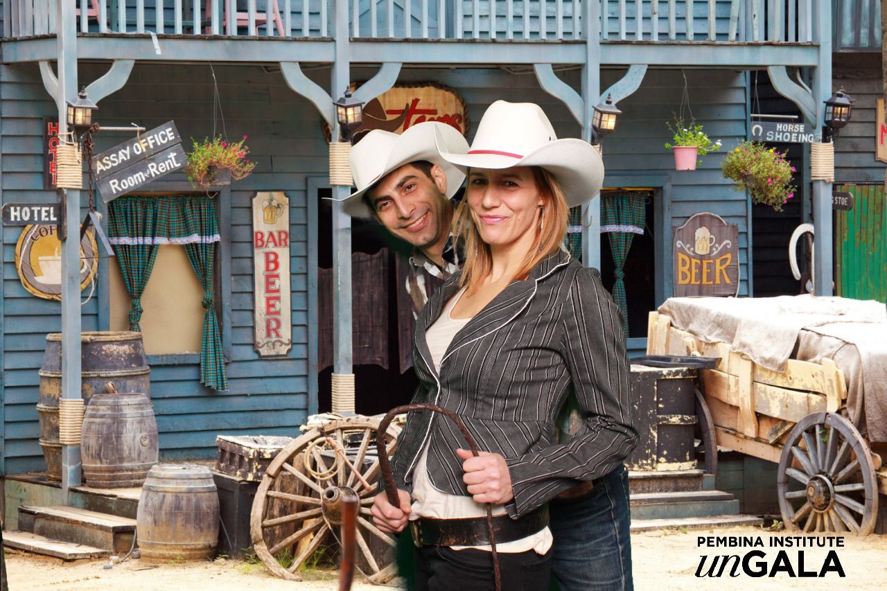 A man and a woman in cowboy hats are standing in front of a greenscreen image of a saloon type building for a western themed event.  Image provided by LOL Photo Booth GTA.