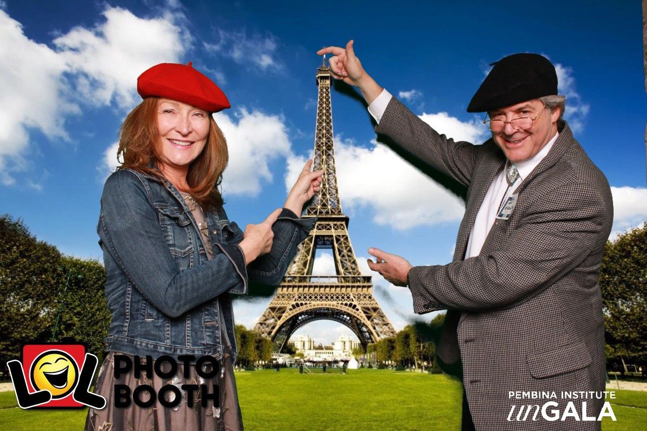 Two people pose in front of Eiffel Tower backdrop, wearing berets and pointing toward the tower.