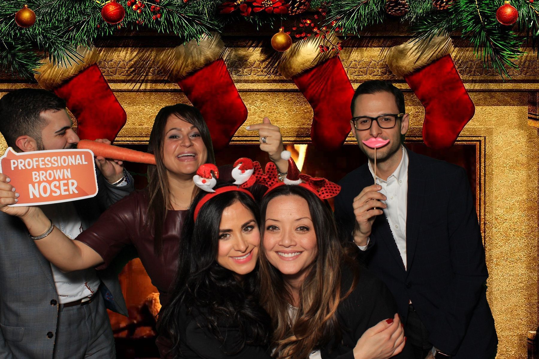 A group of people are posing for a picture in front of a greenscreen image of a fireplace with Christmas stockings.  Image provided by LOL Photo Booth GTA.