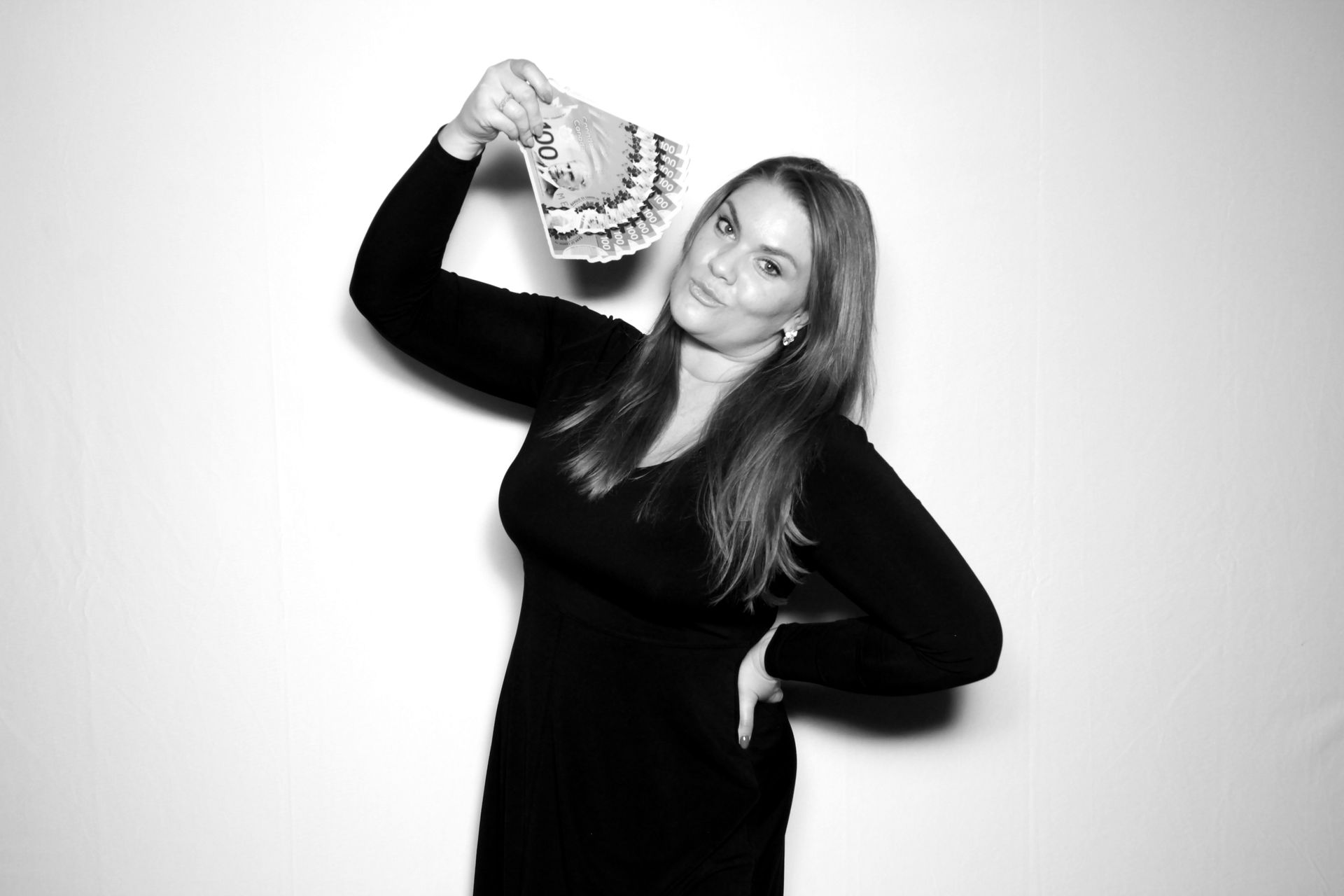 Woman in black dress holding up money, posing in front of a white backdrop.