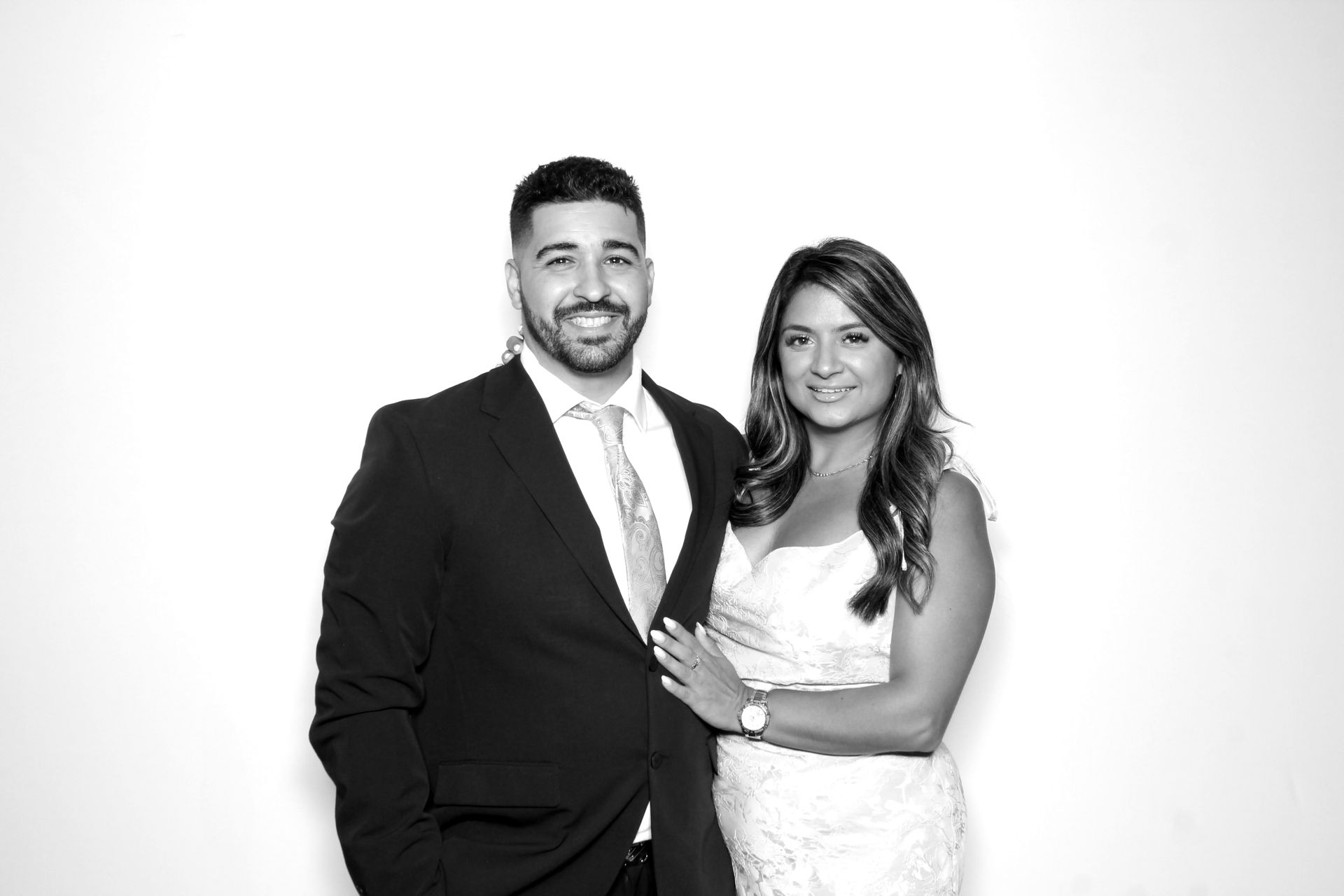 Man in suit and woman in dress smiling, posing for photo against white backdrop.