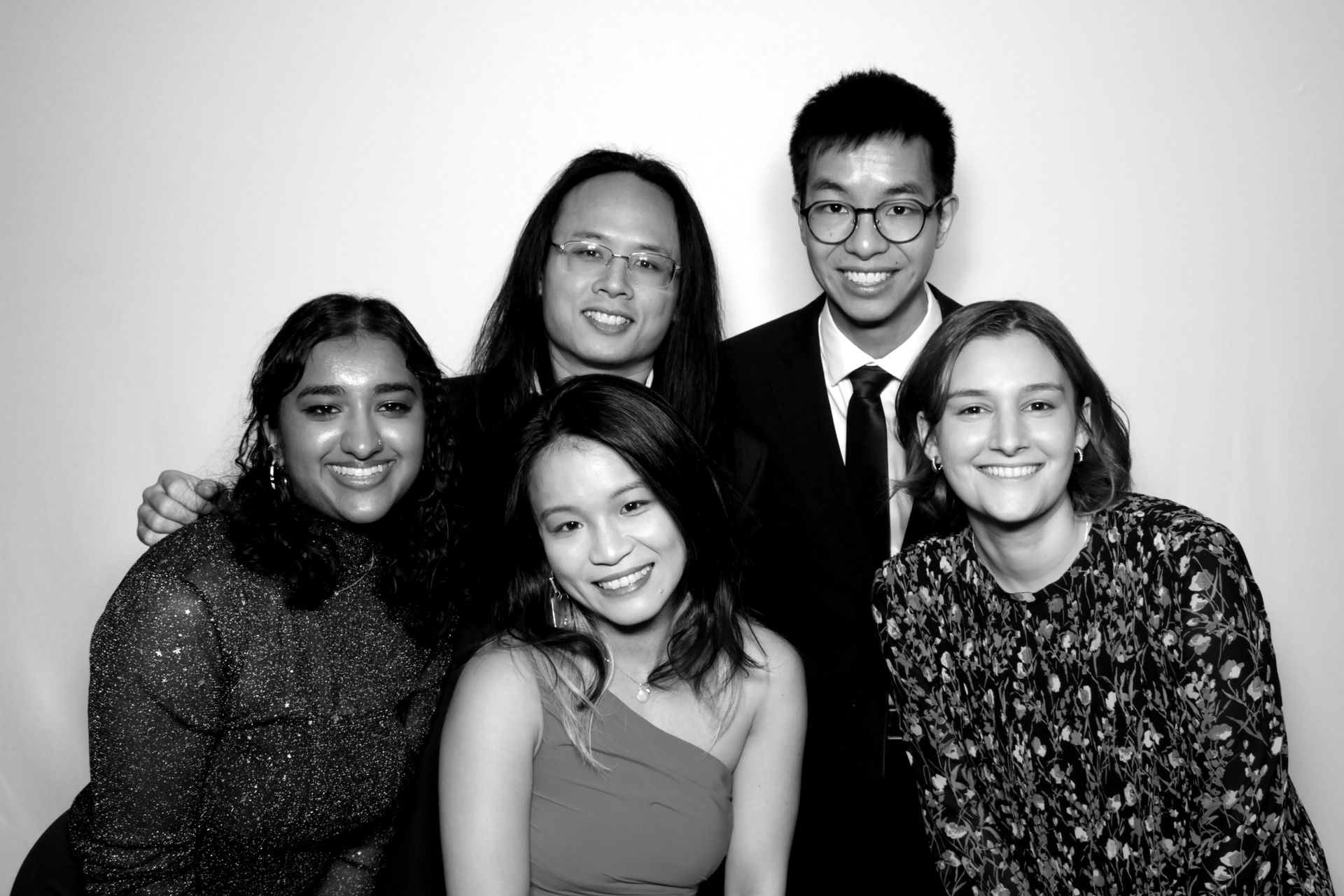 Group of five smiling people posing for a photo against a white backdrop.