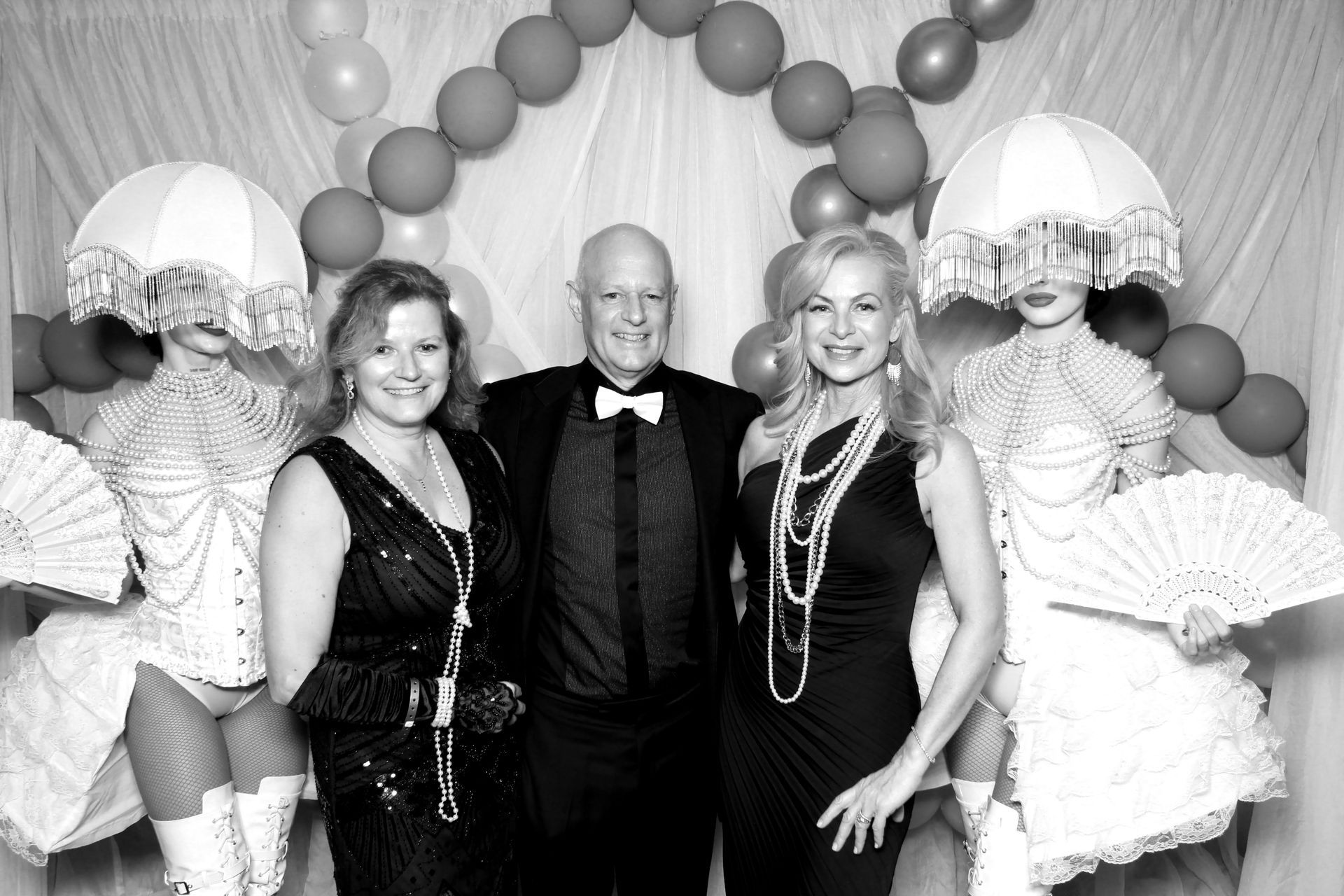 Three people pose with costumed performers at a gala. Red and gray balloons decorate the backdrop.