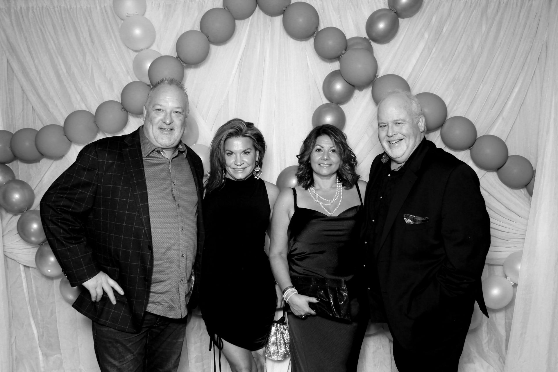Four people pose in front of a white backdrop with balloons. Two women and two men smiling at the camera.
