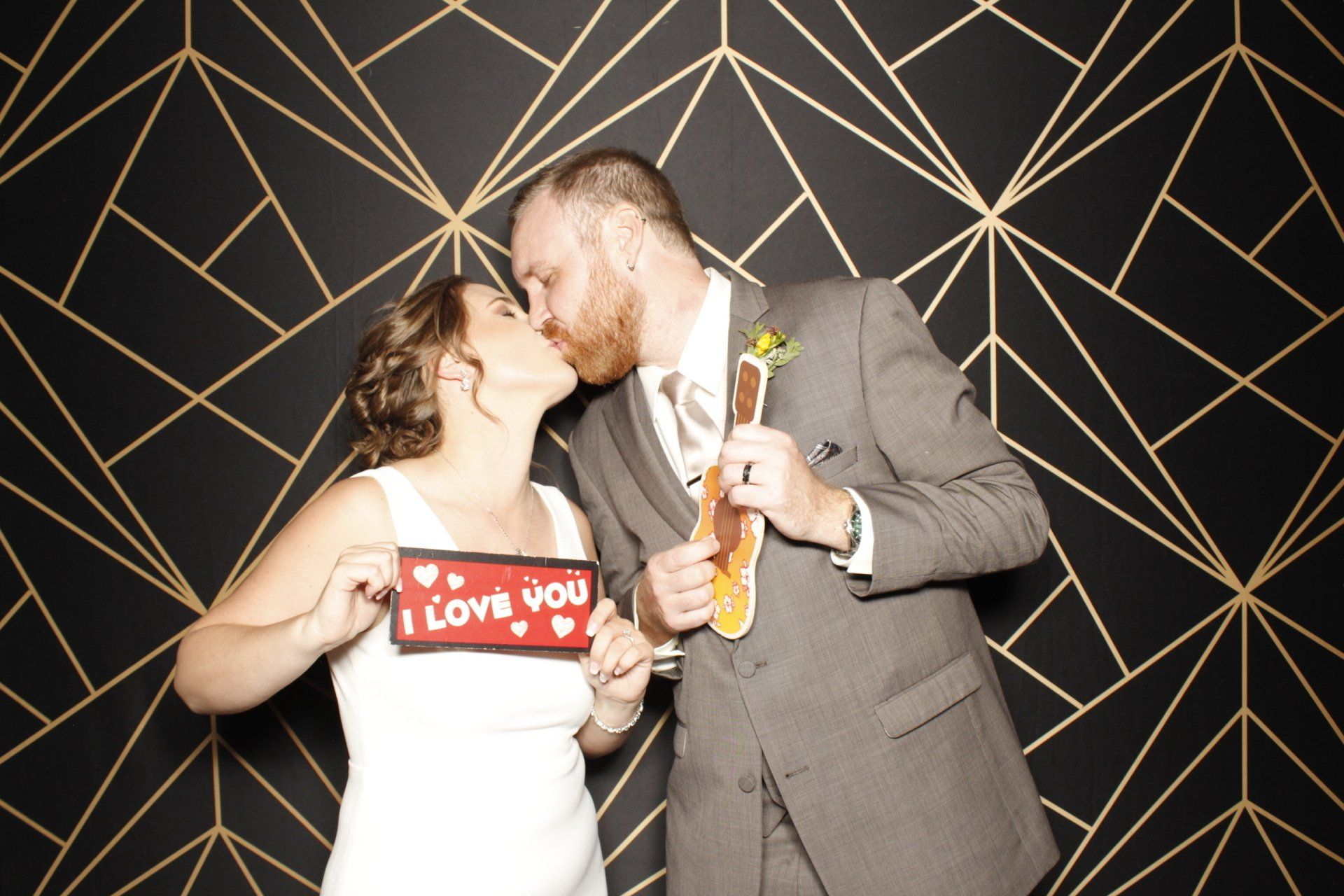 A bride and groom taking a photo booth picture holding prop signs and kissing.