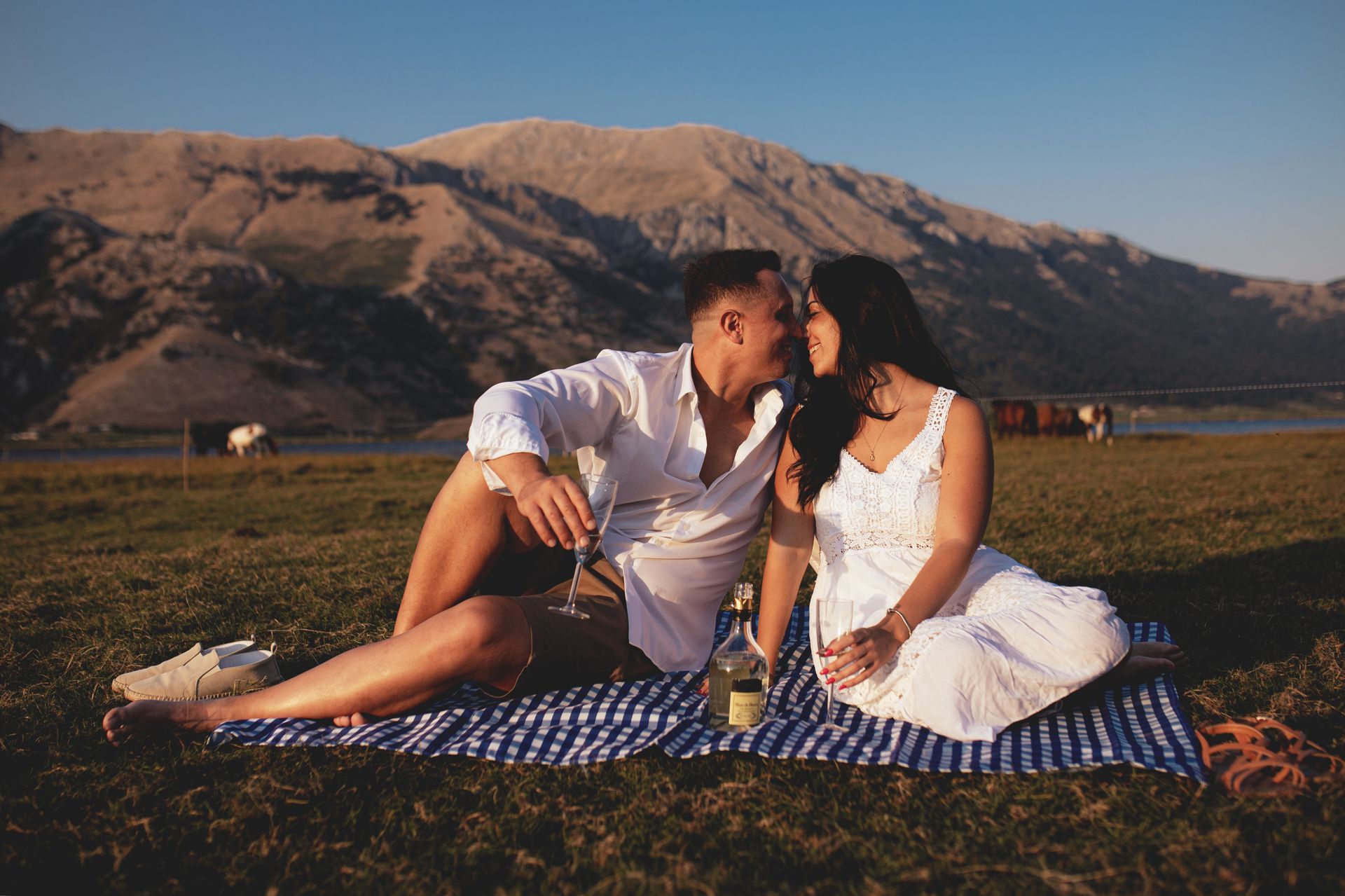 Coppia che si bacia durante un picnic su una coperta a strisce blu, con le montagne sullo sfondo.