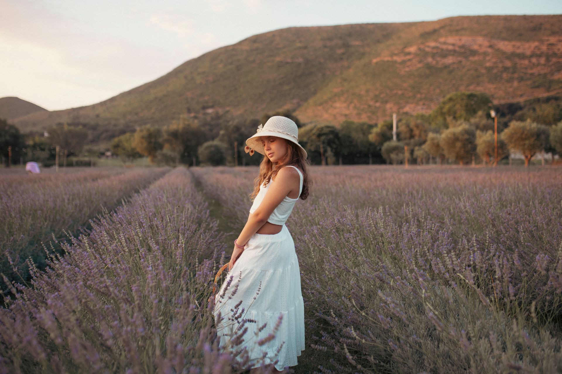 Donna con abito bianco e cappello in un campo di lavanda, con le montagne sullo sfondo.