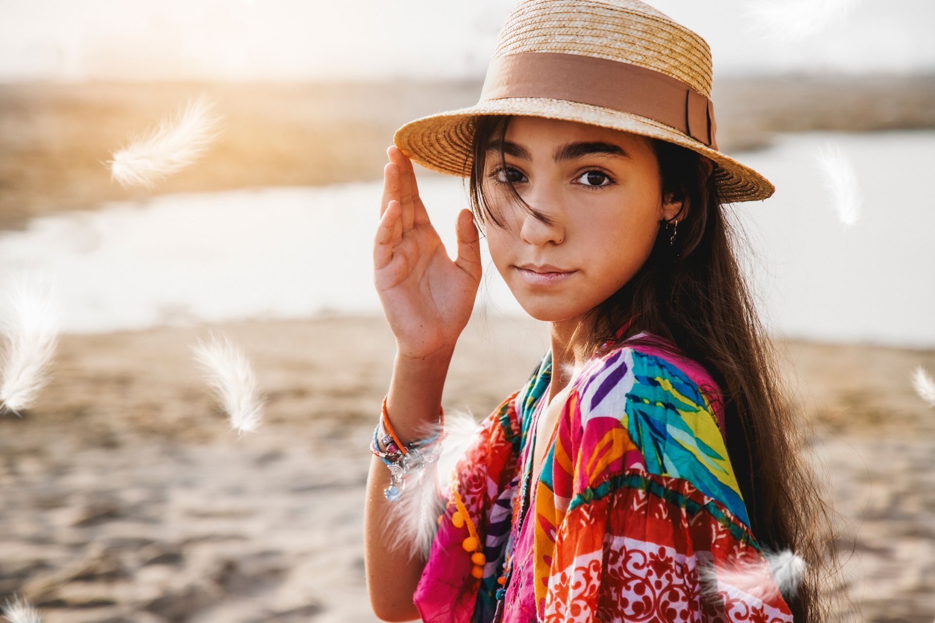 Un giovane indossa un cappello di paglia su una spiaggia, con la mano fino all'orlo e la parte superiore colorata.