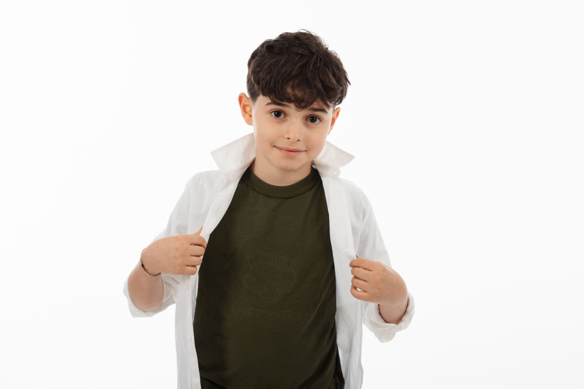 Ragazzo con camicia bianca sbottonata sopra una camicia verde, che guarda l'osservatore.