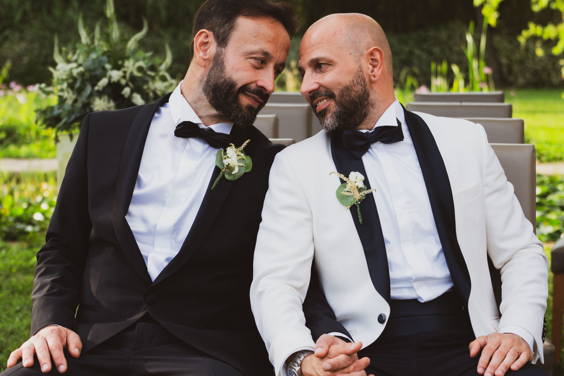 Due uomini in smoking si tengono per mano e si guardano con adorazione all'aperto.