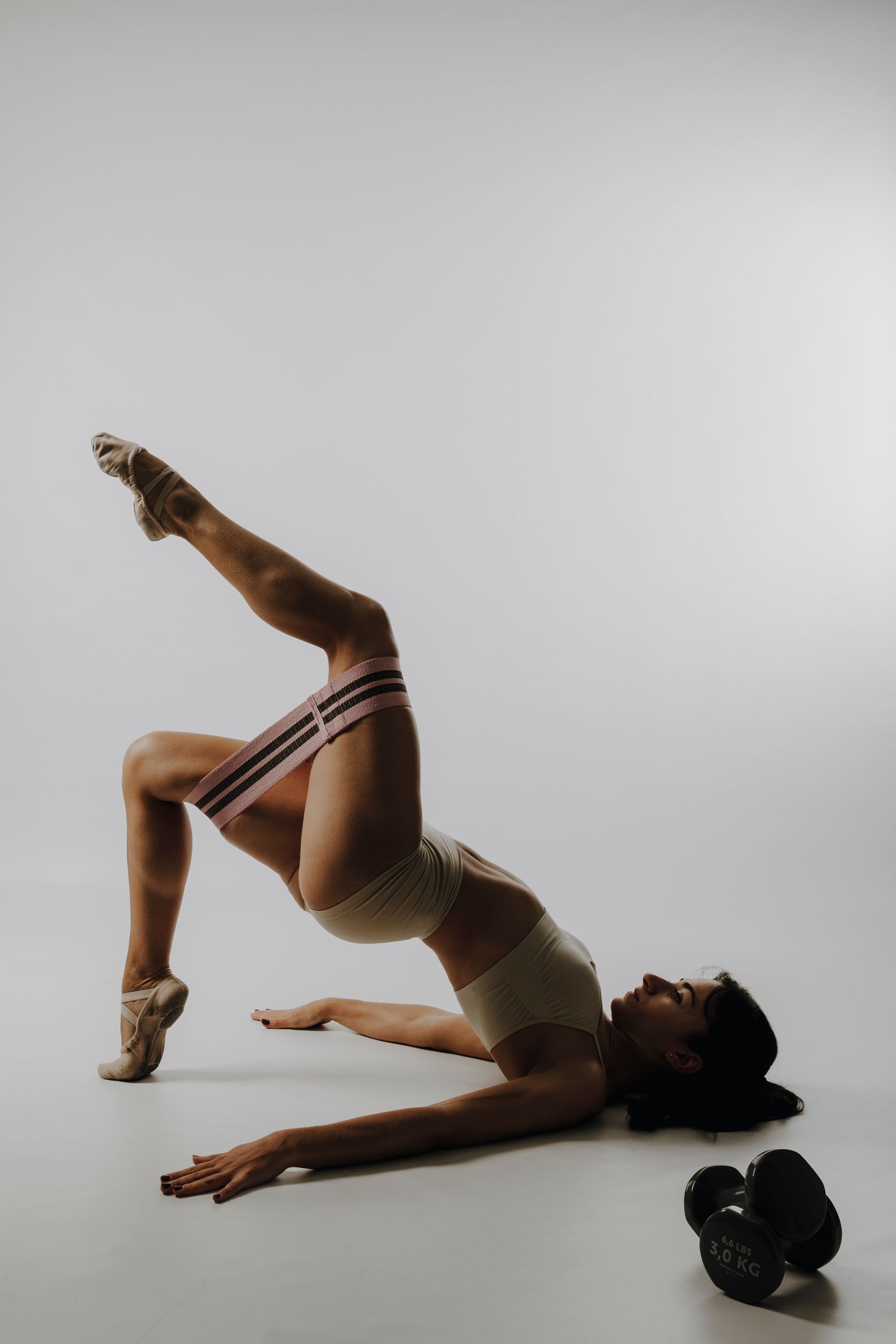 Donna in tenuta da ginnastica che esegue l'esercizio del ponte con una gamba sollevata, fascia di resistenza e un peso.
