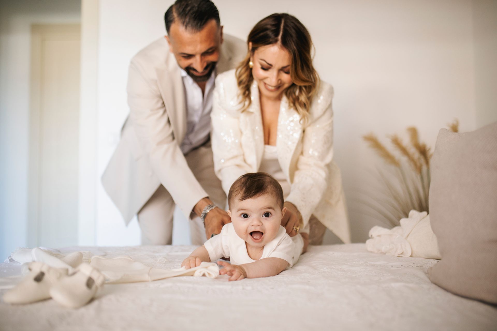 I genitori si chinano su un neonato sdraiato sul letto. Il neonato sorride, mentre i genitori lo guardano amorevolmente.