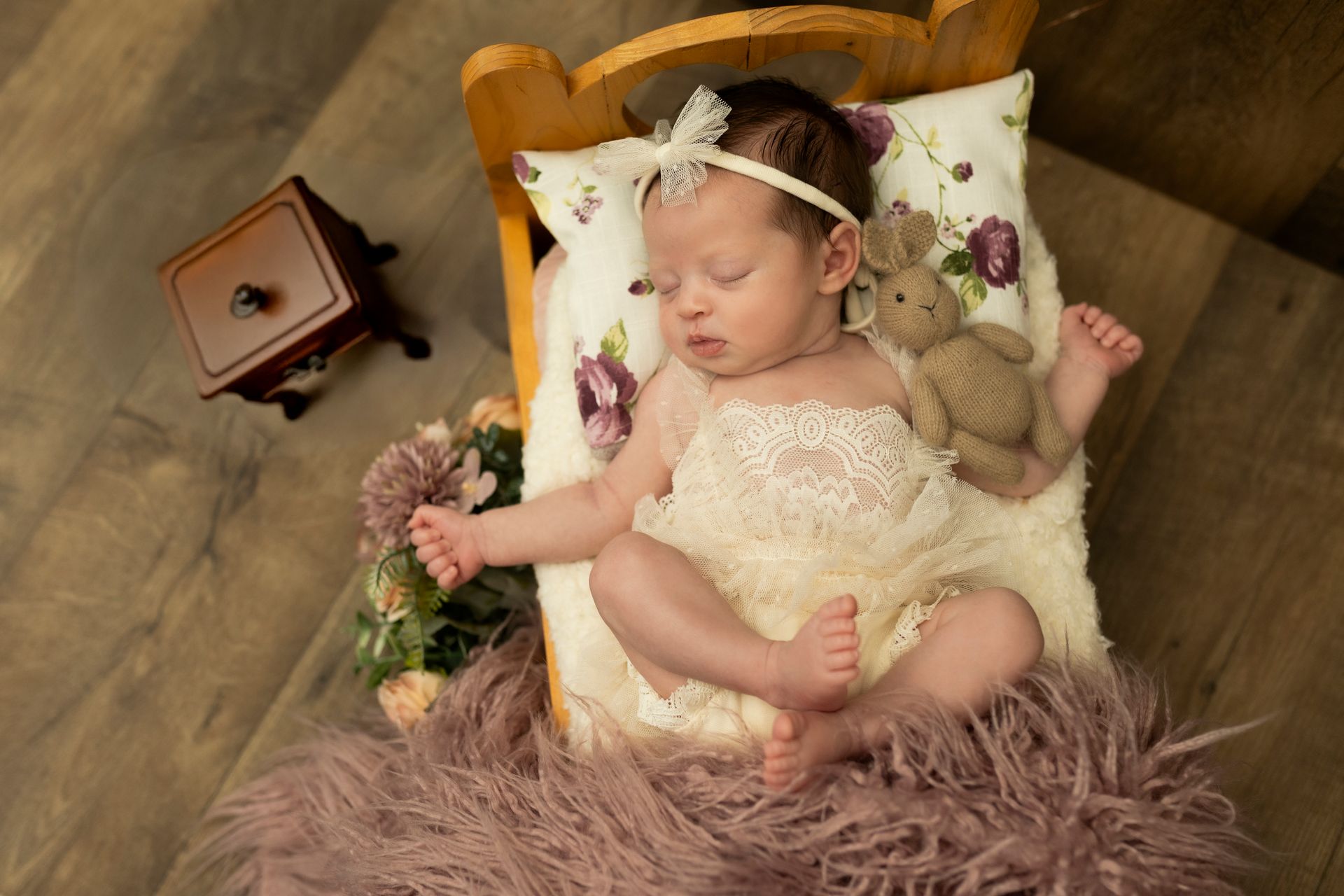 Neonato che dorme in un lettino di legno con un peluche e un cuscino floreale.