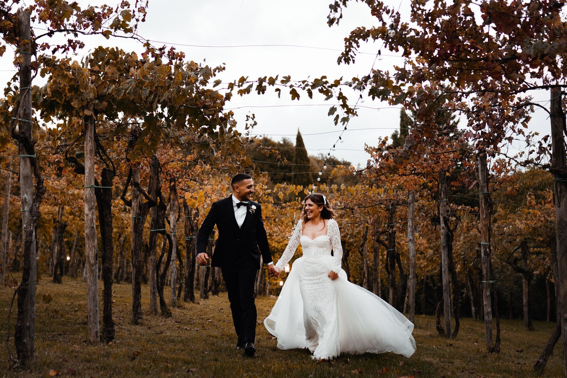 Una coppia in abito da sposa si tiene per mano e cammina attraverso il vigneto.