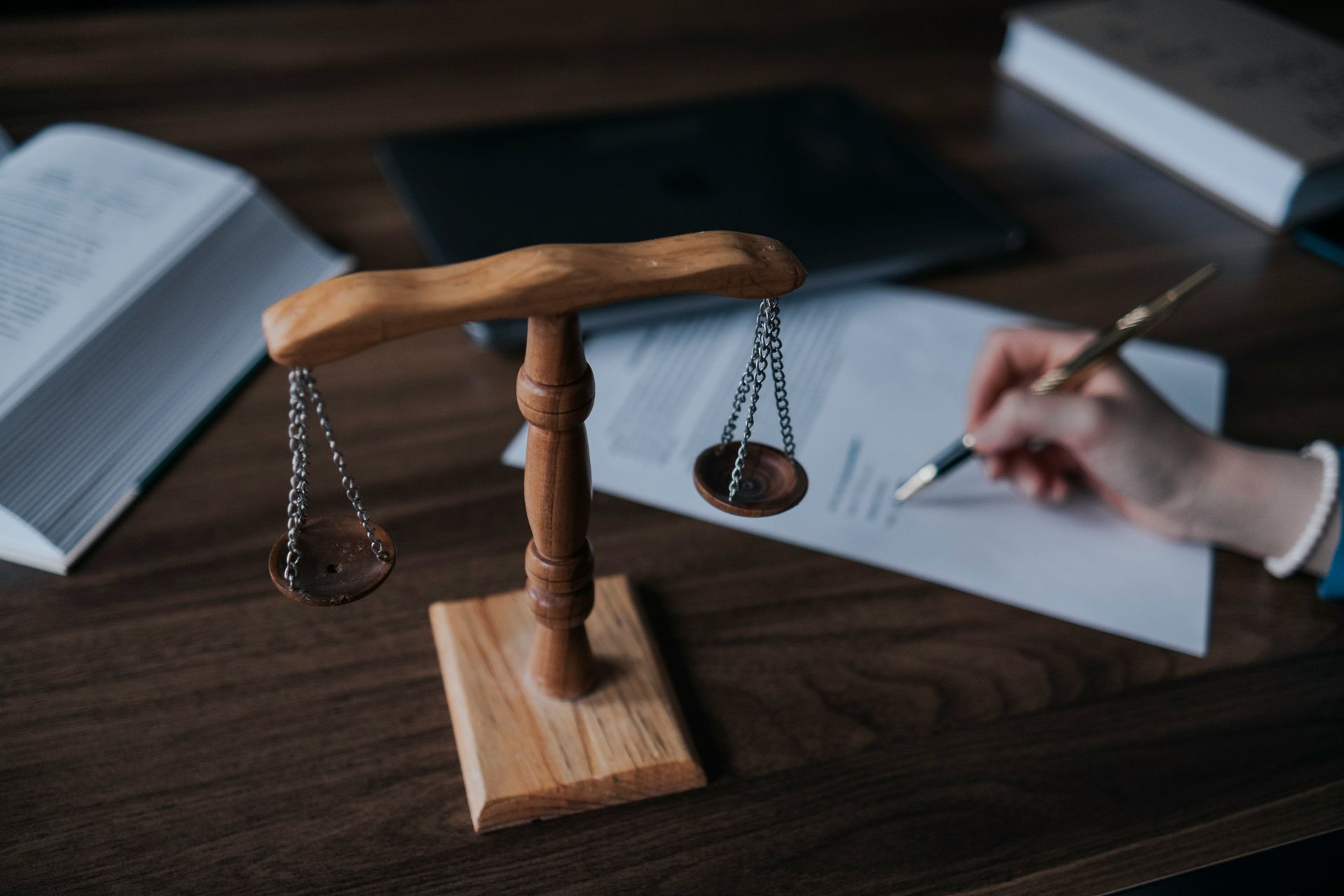 Wooden scales of justice on a desk with books and a person signing a document.