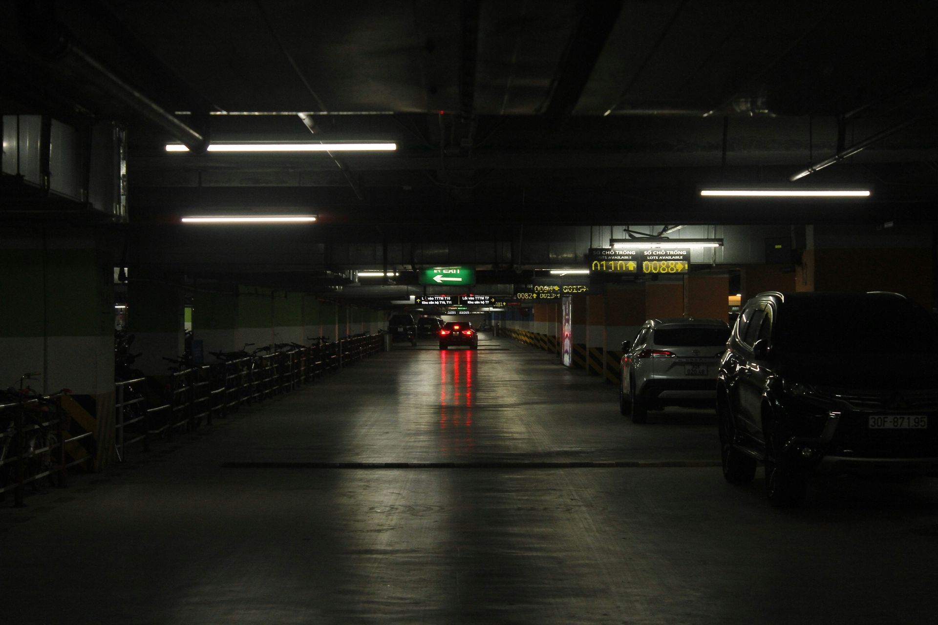 Dark parking garage with a car driving toward the camera; red taillights are visible.