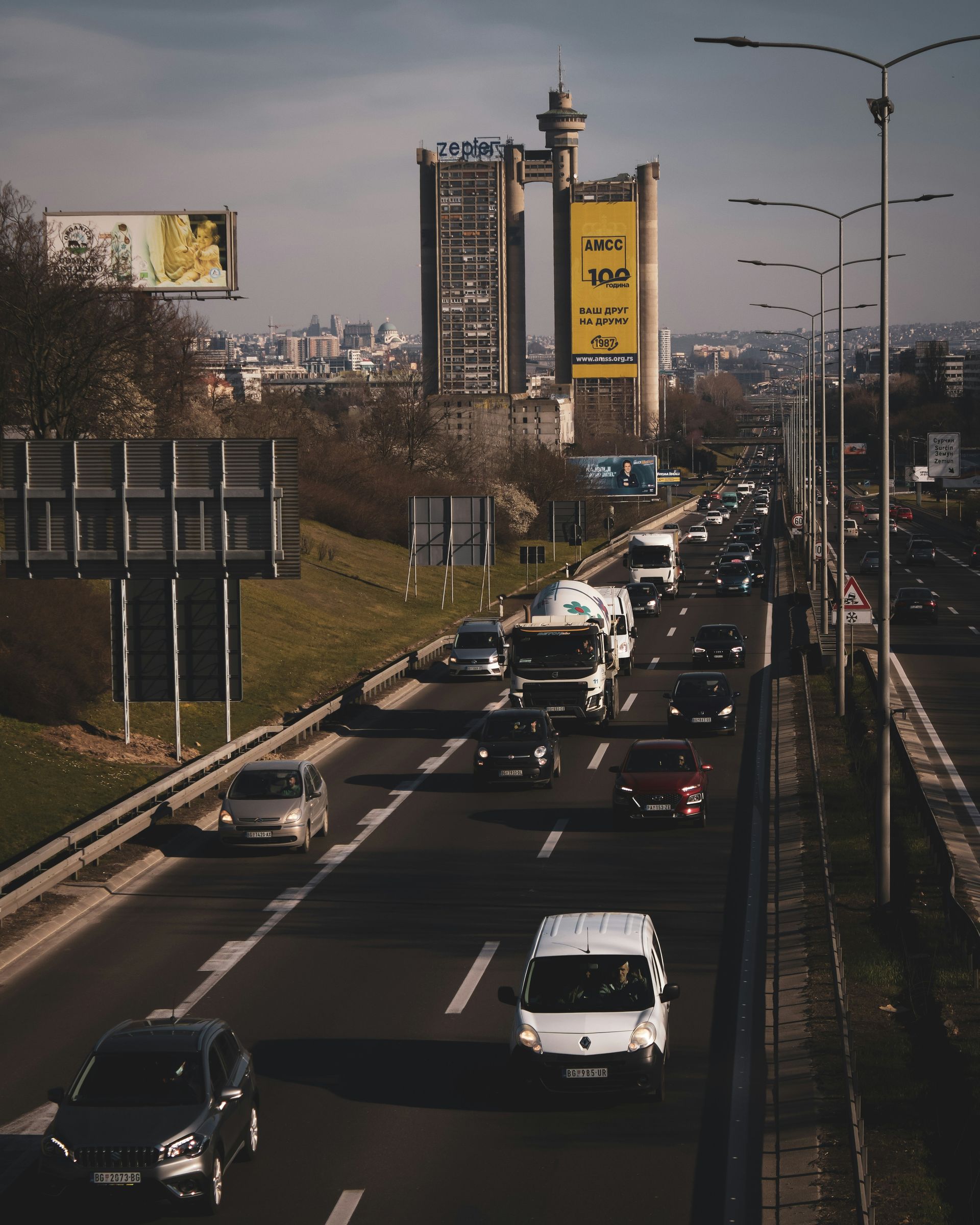Busy highway with cars and trucks, cityscape in the background, tall building with advertising on the right.