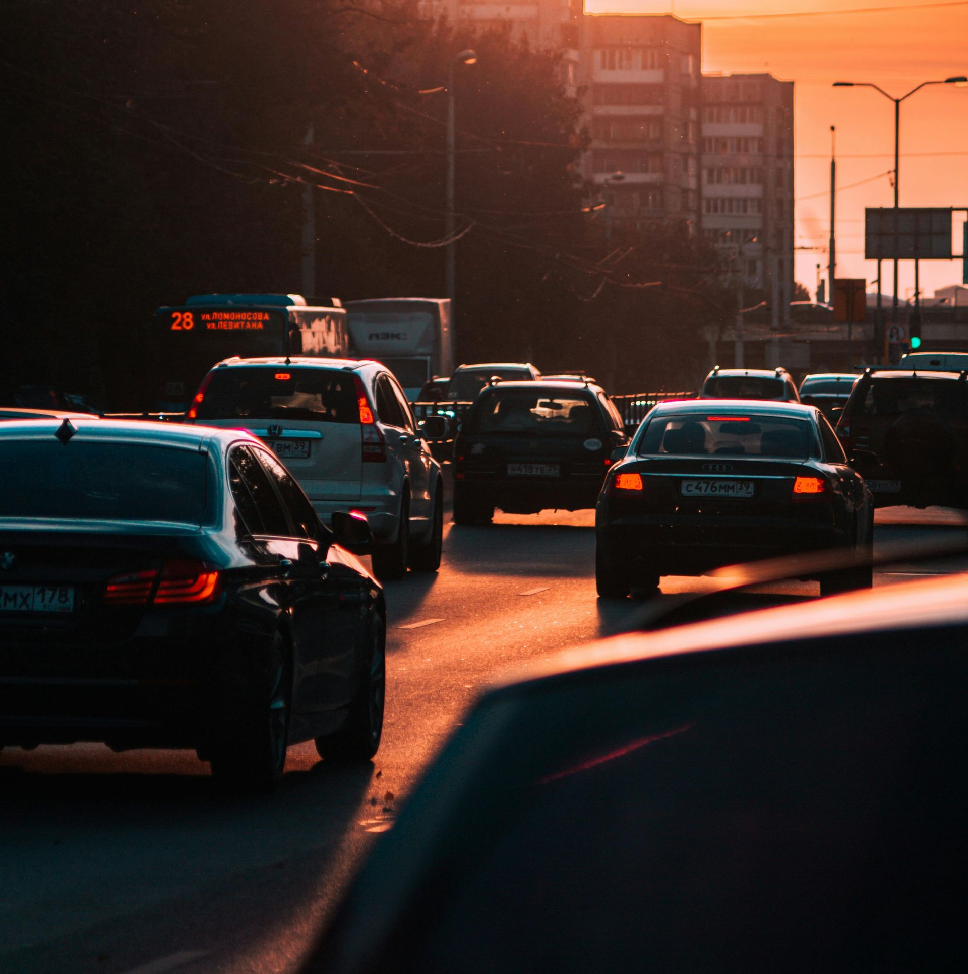 Cars in traffic on a city street at sunset, silhouetted against an orange sky.