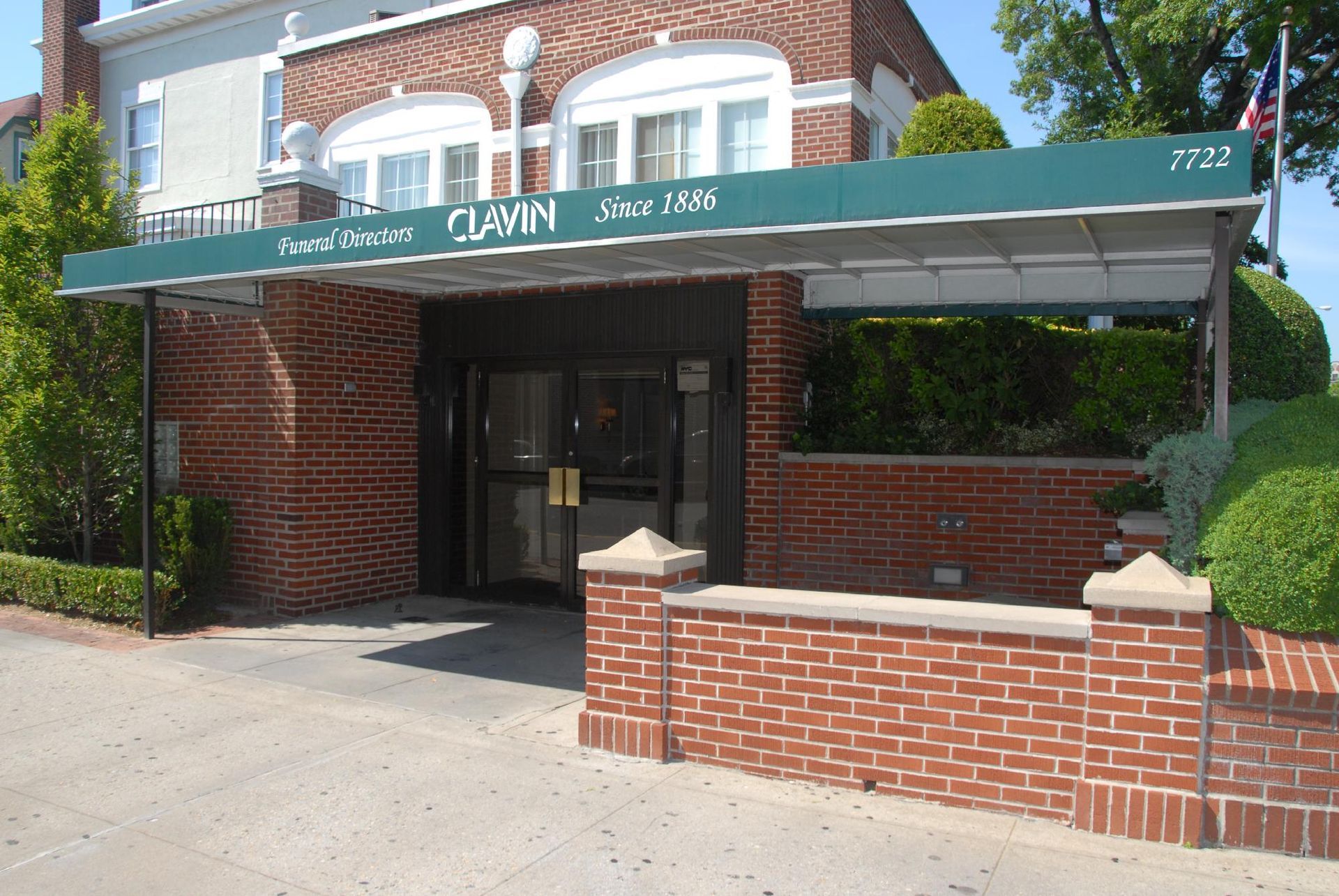 Clavin Funeral Home. Red brick entrance, green awning, glass doors. Building with greenery.