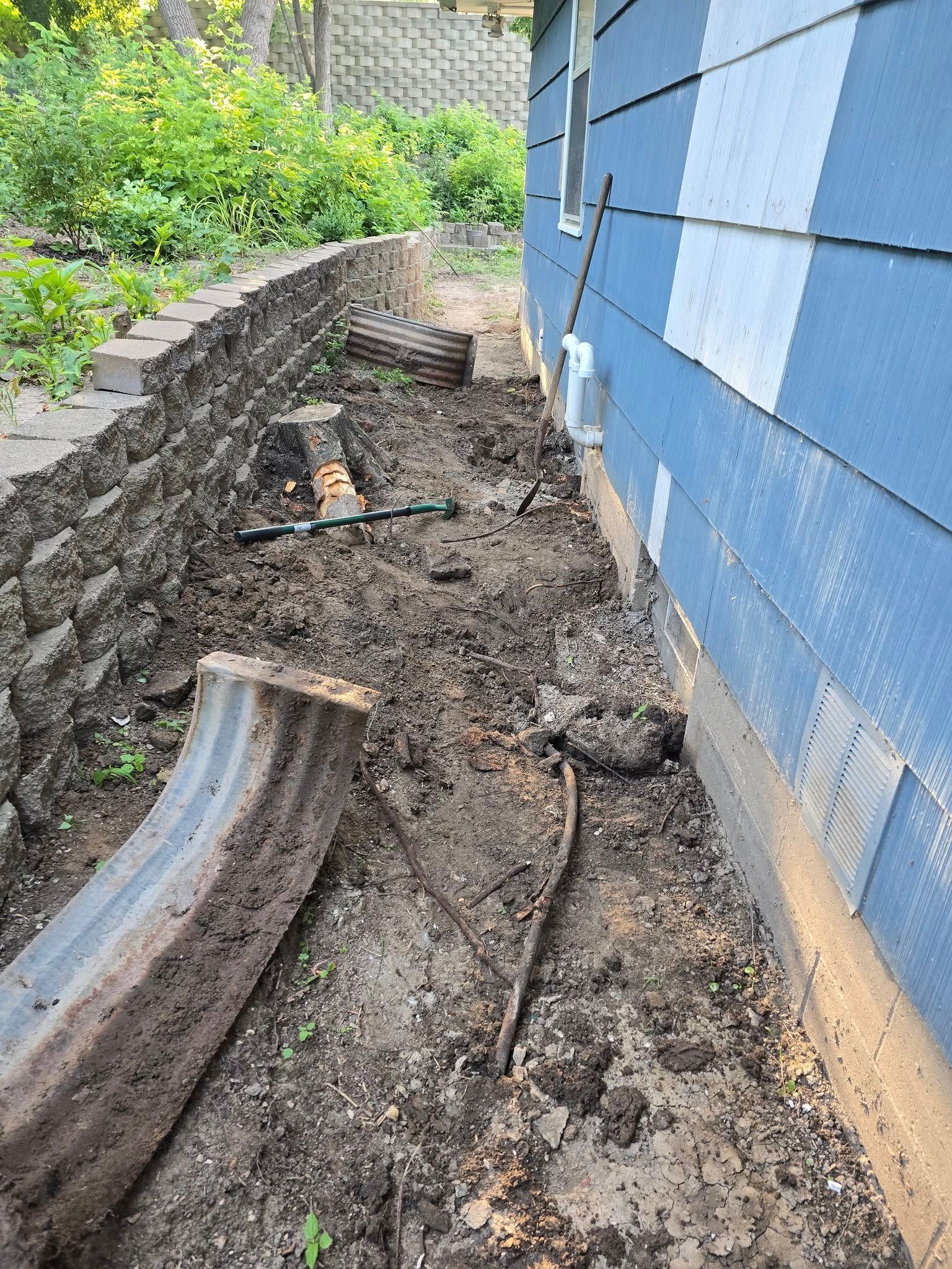 Exterior view with a retaining wall, bare earth, a corrugated metal window well, and blue siding.