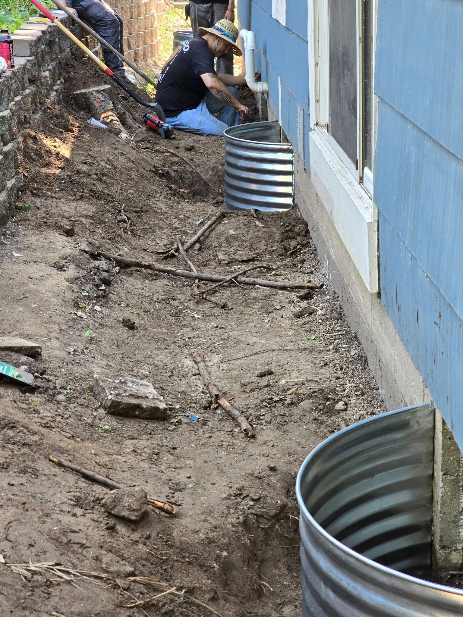 Man installing window well in a trench beside a blue house.