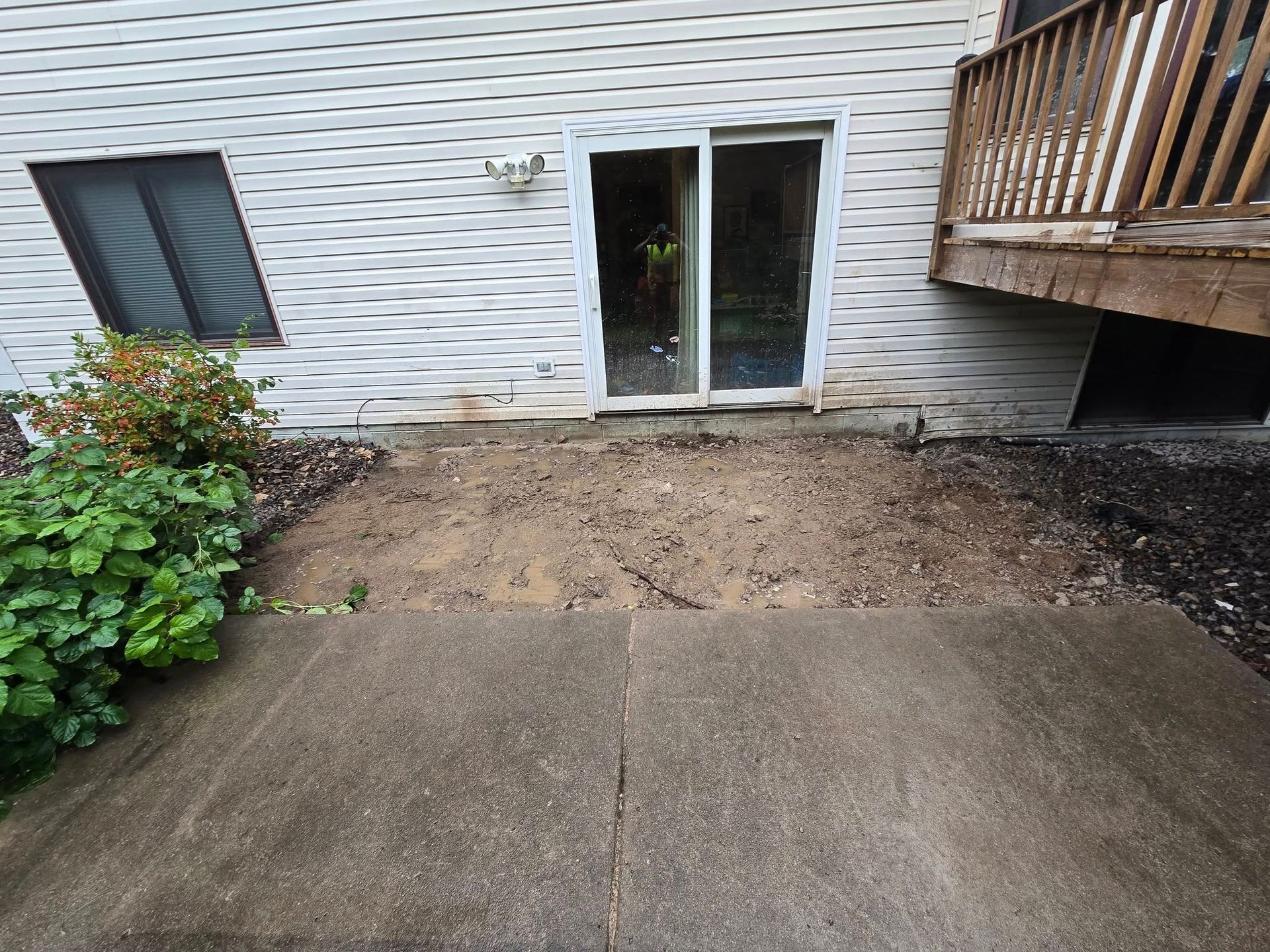 Concrete patio with dirt area in front of a sliding glass door and the base of a deck.