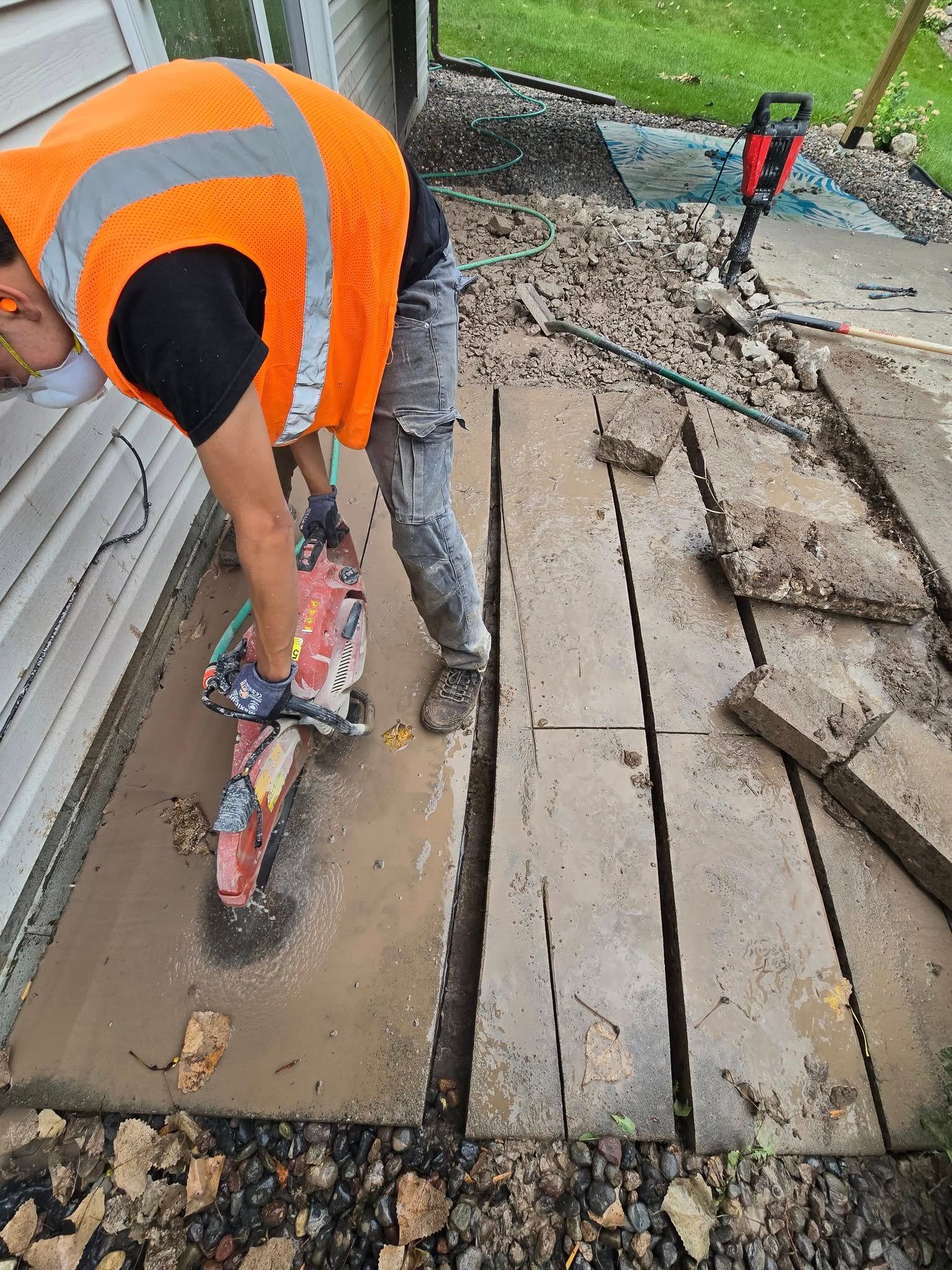 Person in orange vest cutting concrete slabs with a power saw outdoors.