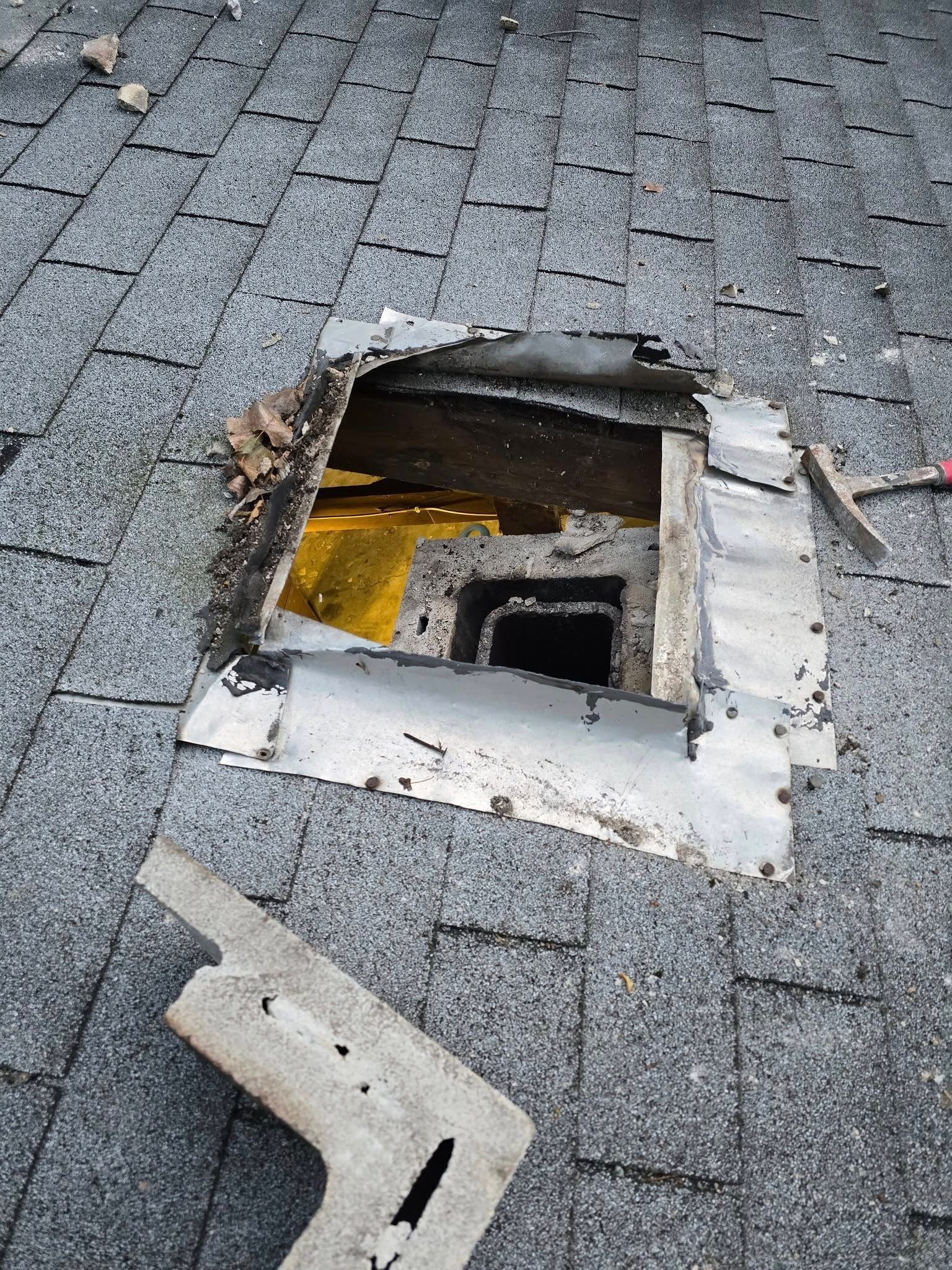 Hole in a gray shingled roof with damaged flashing, revealing the interior structure below.