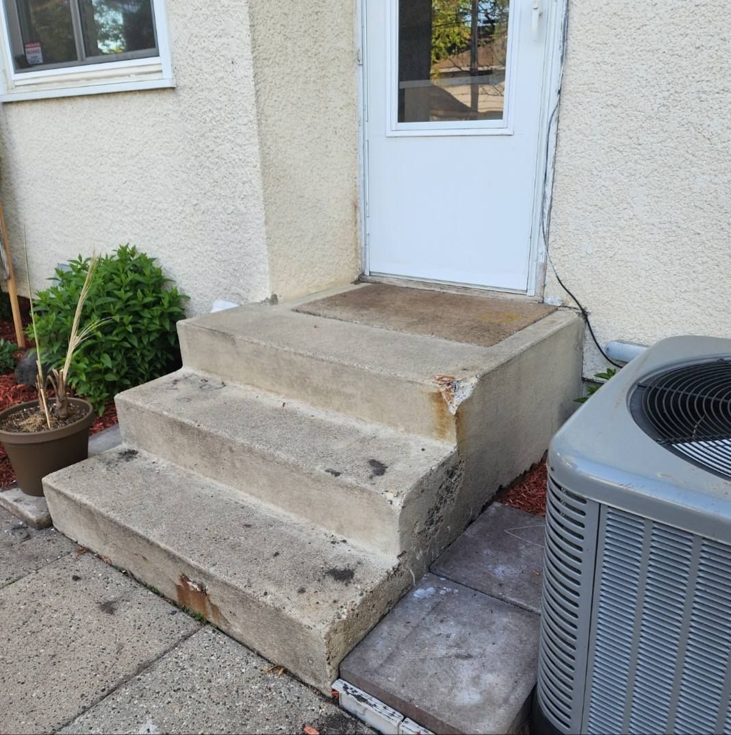 Concrete steps leading to a white door, with an air conditioning unit to the right.