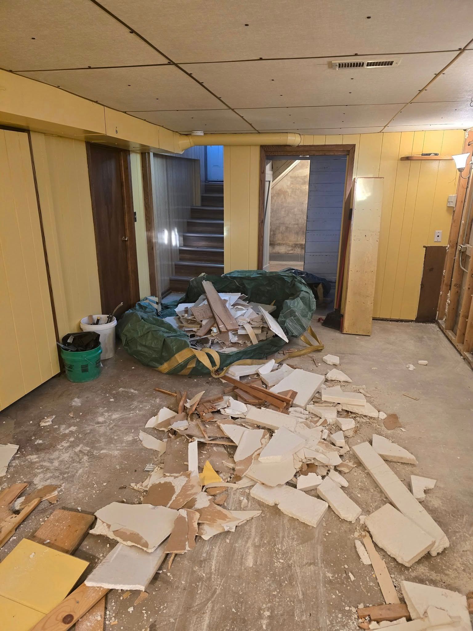 Basement undergoing renovation; debris scattered on floor, contractor bag in center, doors, and stairs visible.