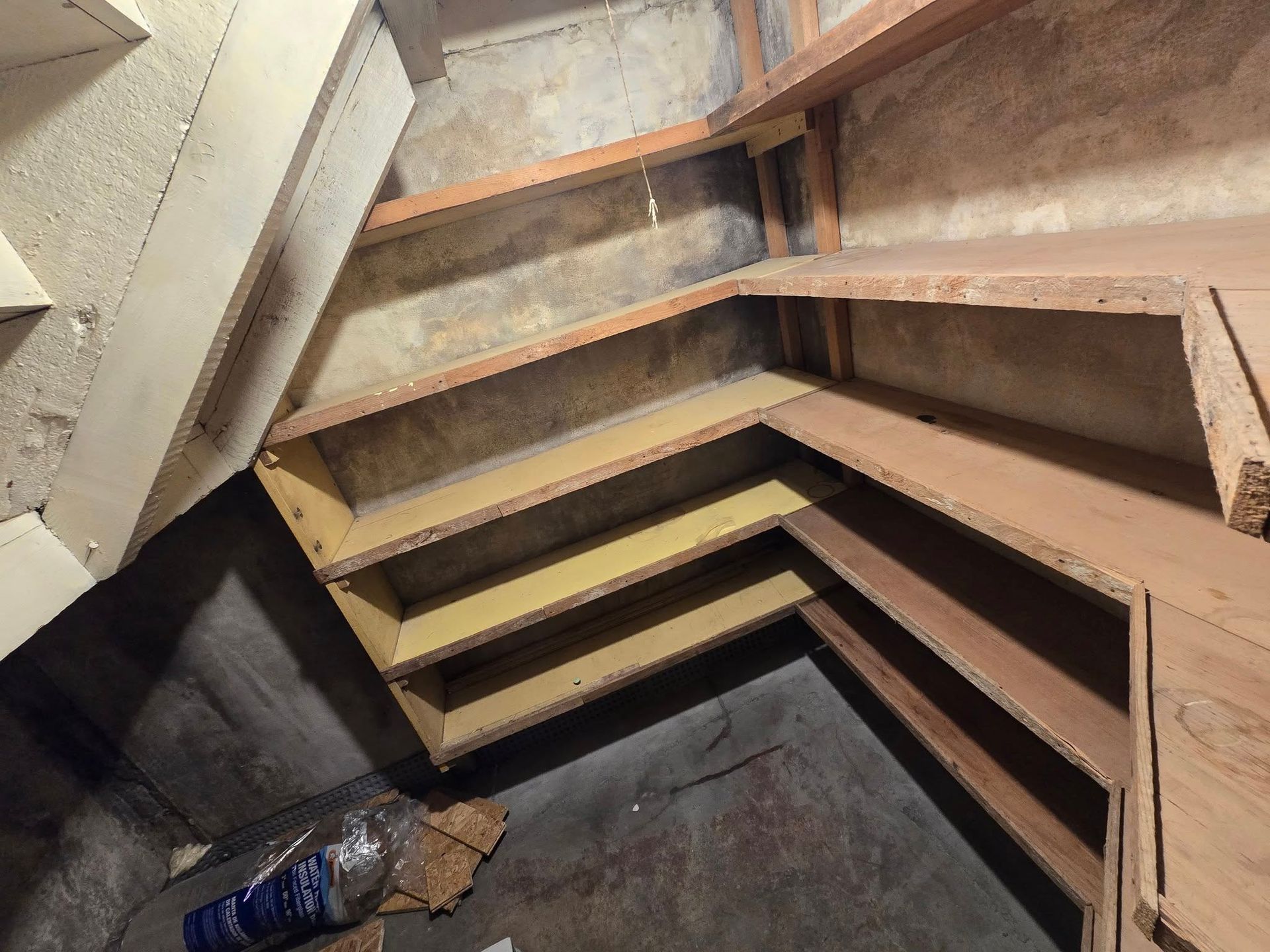 Built-in wooden shelves in a corner, various levels and depths, against a textured wall.