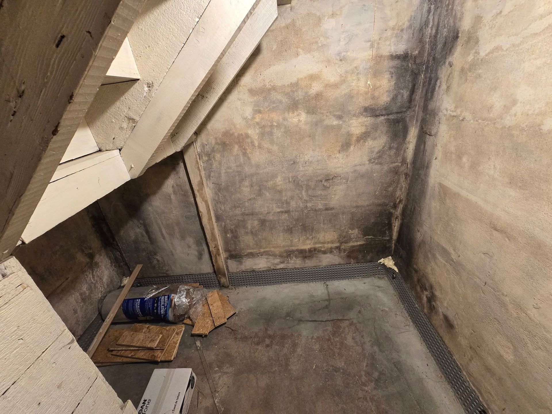 Concrete basement walls with mold and a staircase, with debris on the floor.