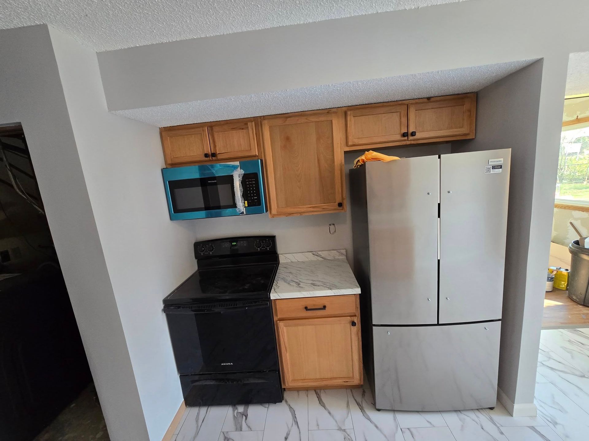 Small kitchen with black stove, light wood cabinets, and stainless steel refrigerator.