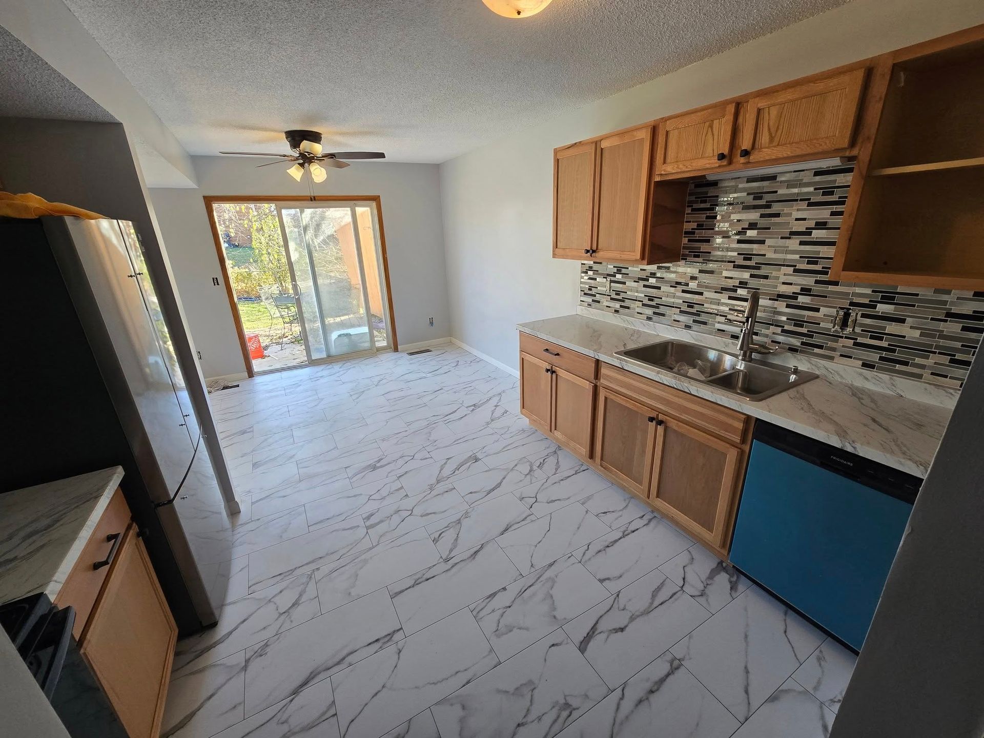 Kitchen with light wood cabinets, gray countertops, and marble-look floor; a blue dishwasher is in view.