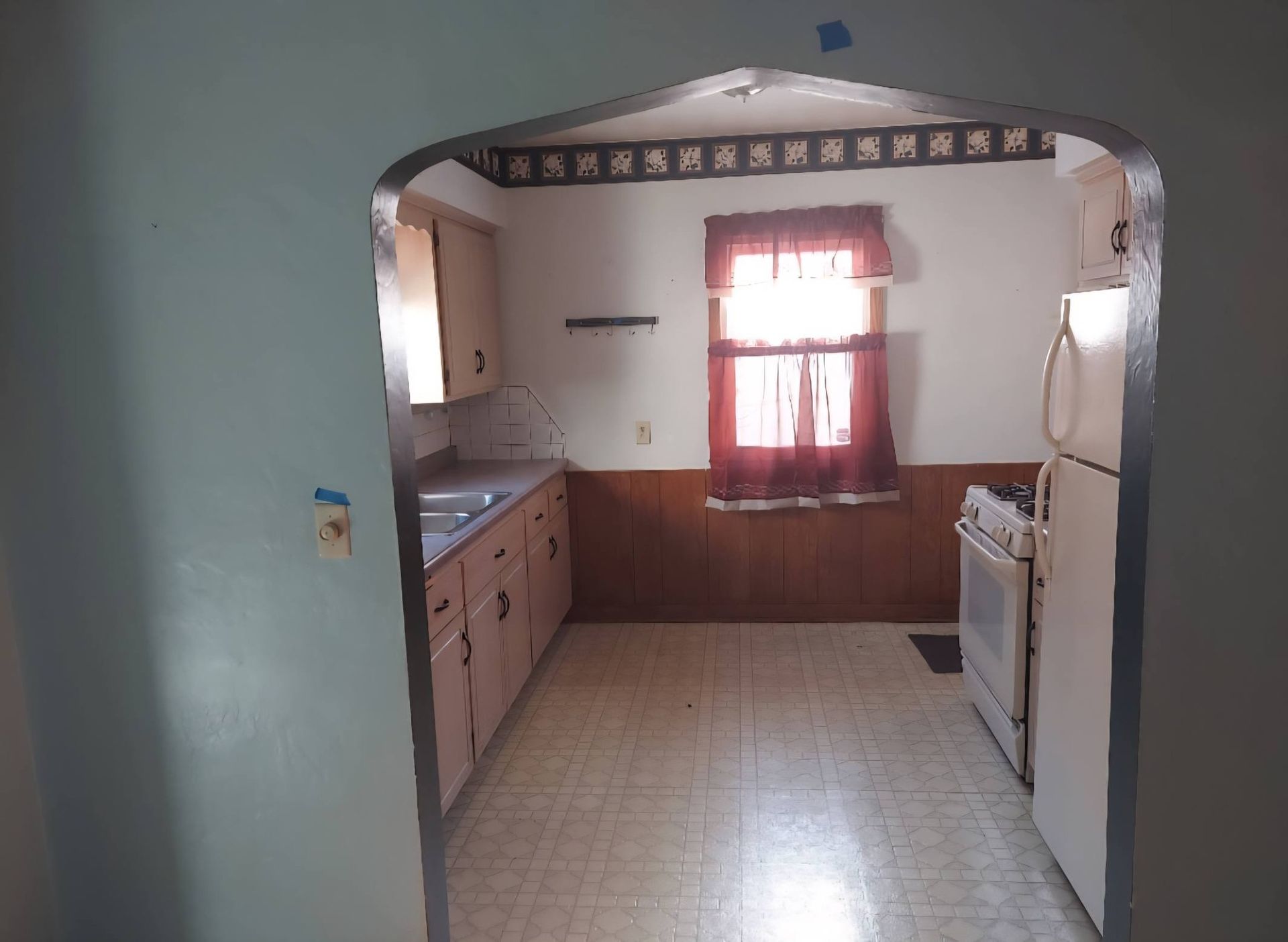 View of a small kitchen with cabinetry, appliances, and a window; the doorway is an arch.