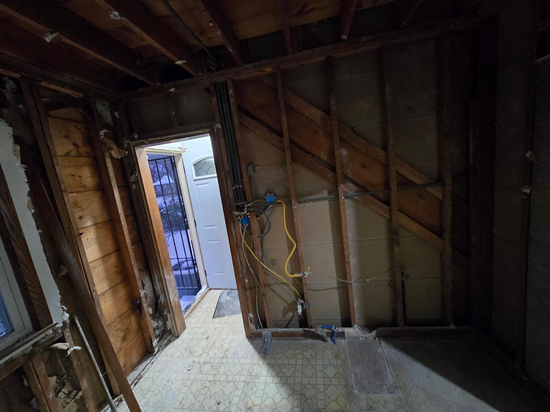 Interior room undergoing renovation, exposed studs and doorway. Yellow electrical wire visible.