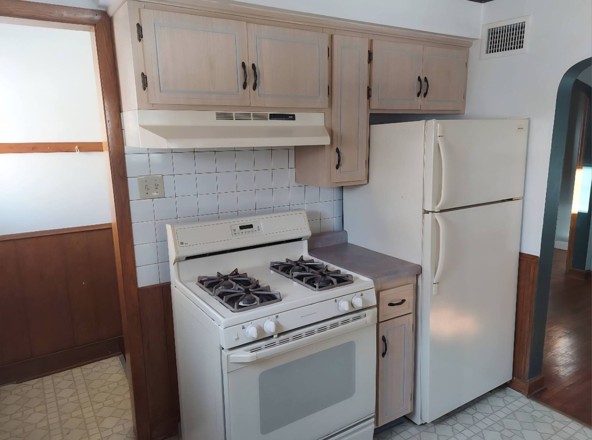 Kitchen with white appliances: stove, refrigerator, and cabinets. Pale brick backsplash.