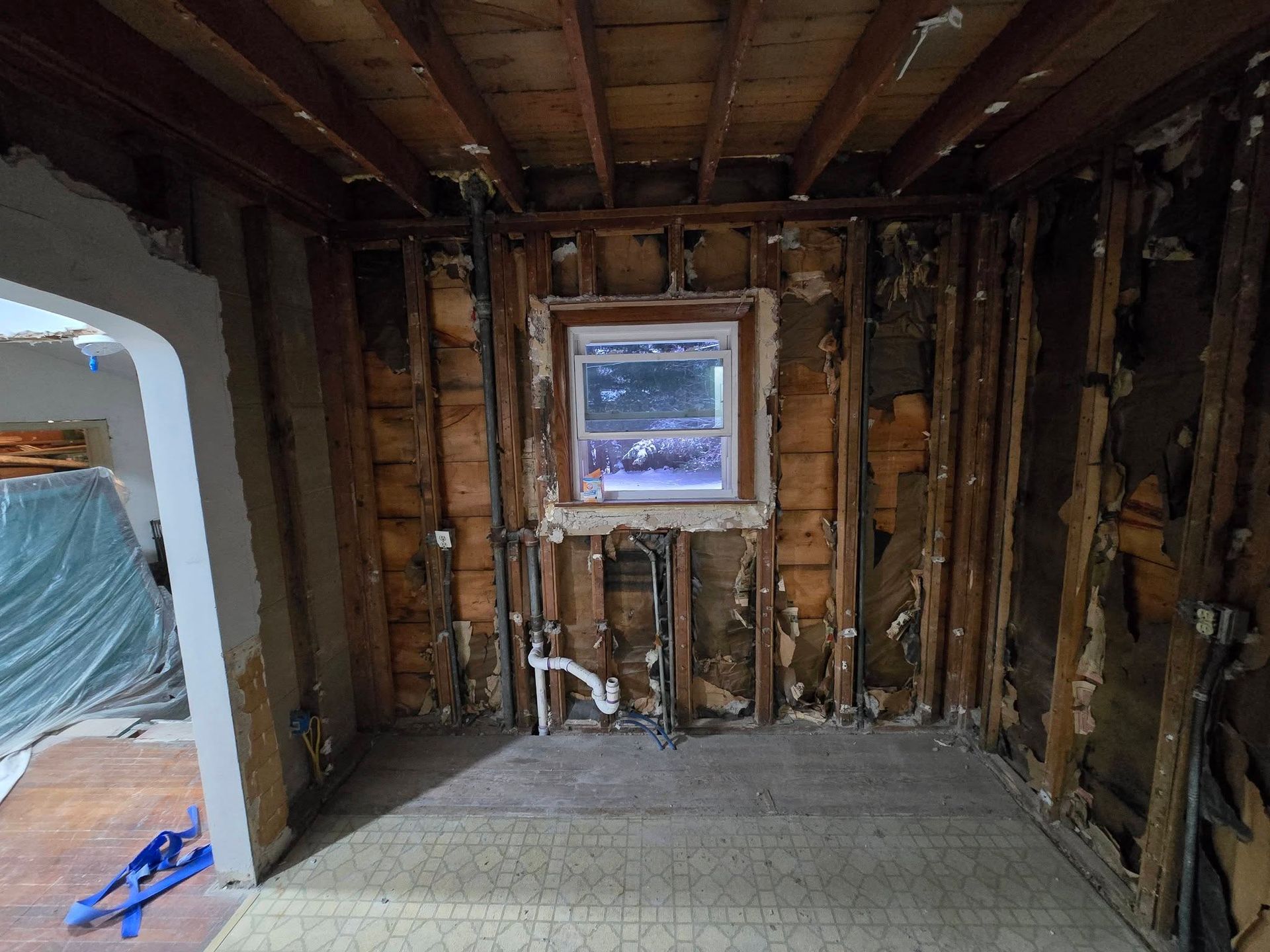 Room under renovation; walls stripped to studs. Window visible, plumbing exposed.