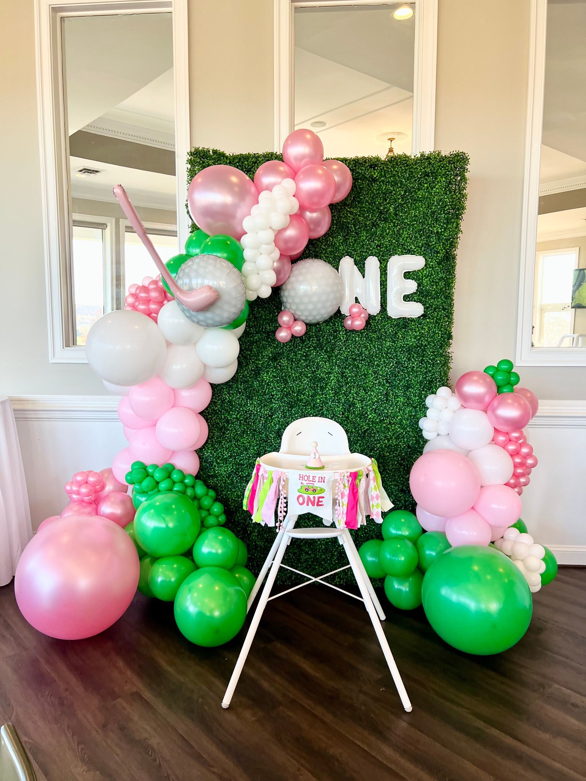 A high chair is decorated with pink and green balloons for a first birthday.