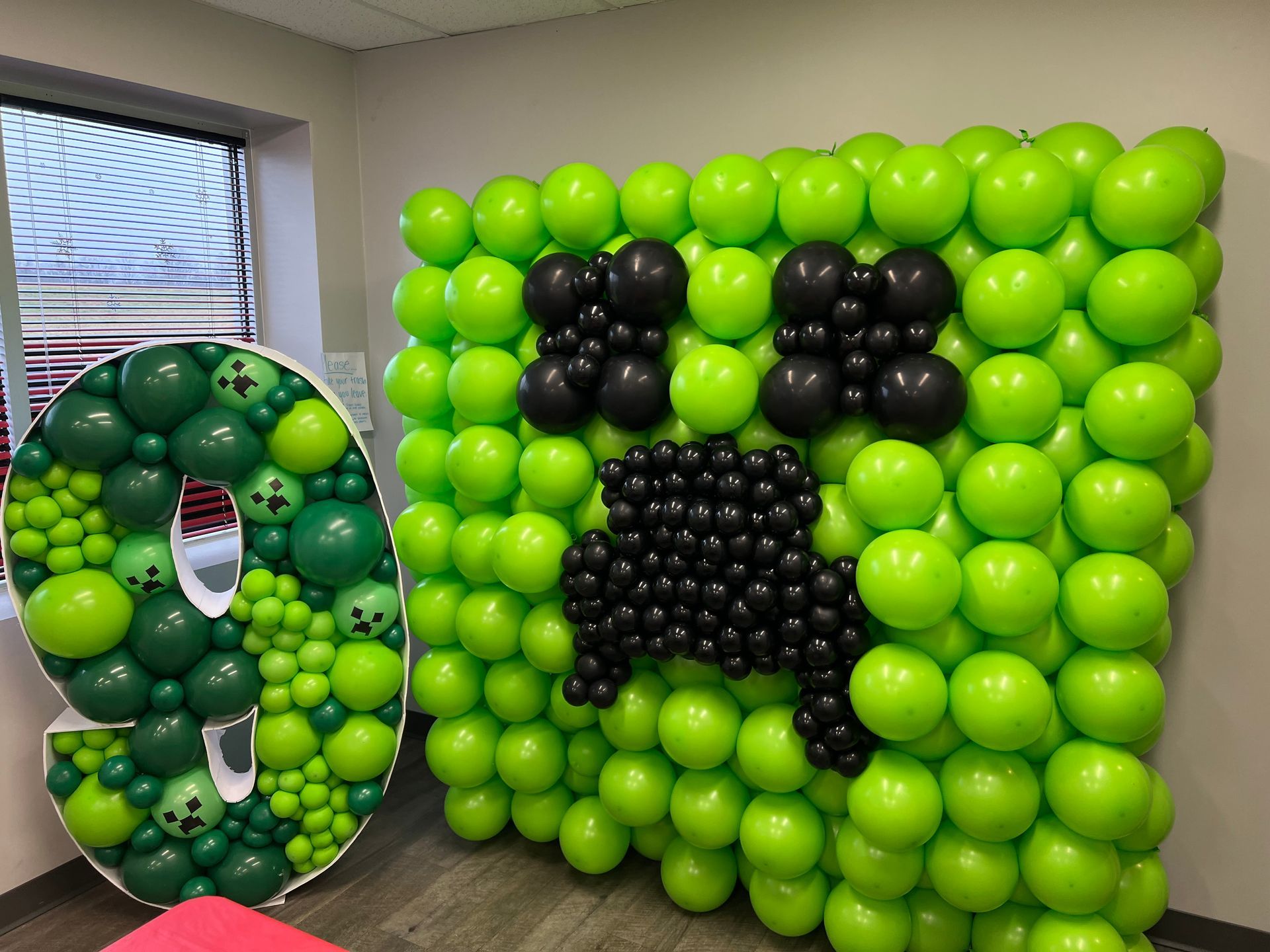 A wall made of green and black balloons with a creeper on it.