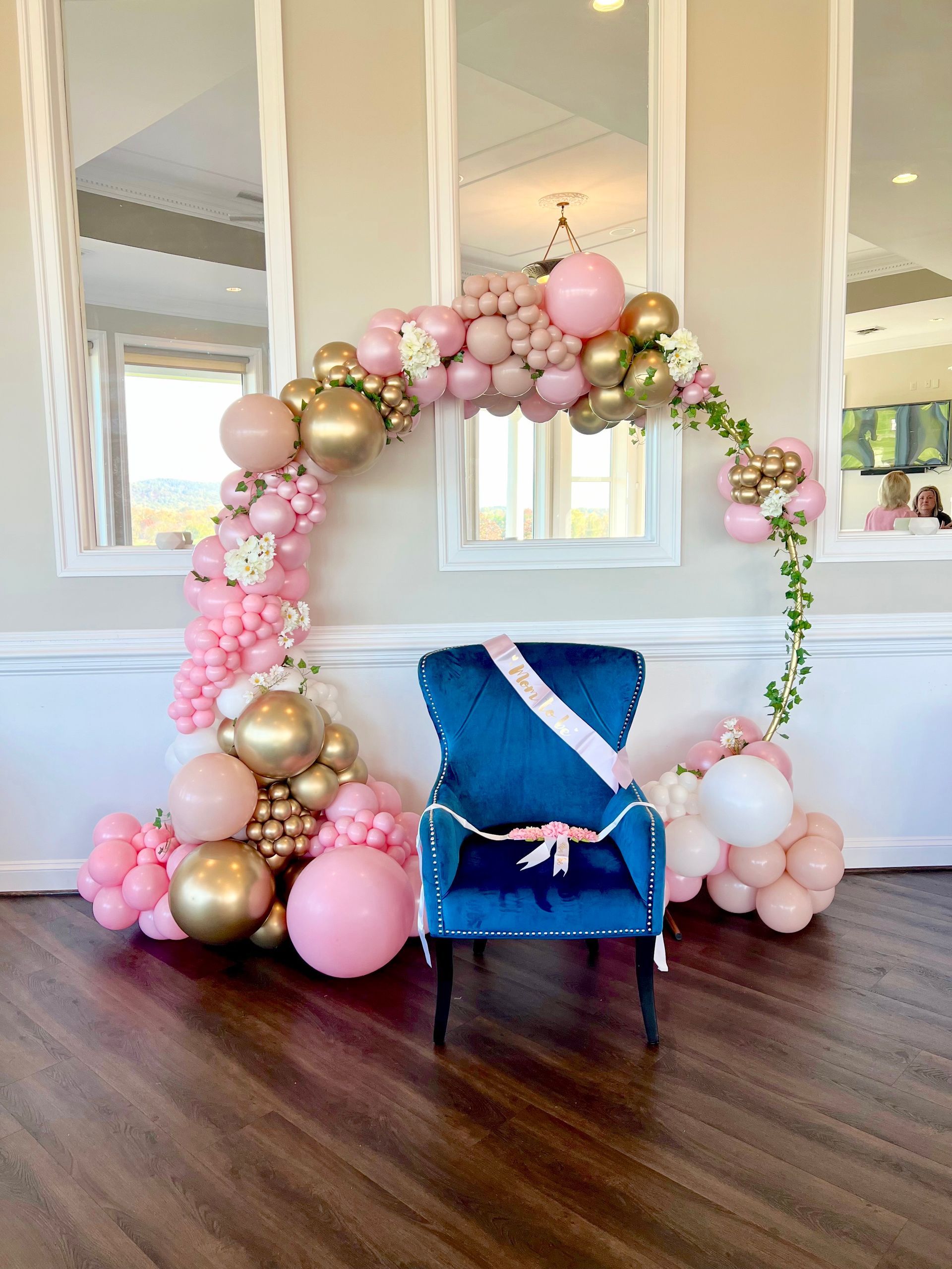 A chair is sitting in front of a wall decorated with pink and gold balloons.
